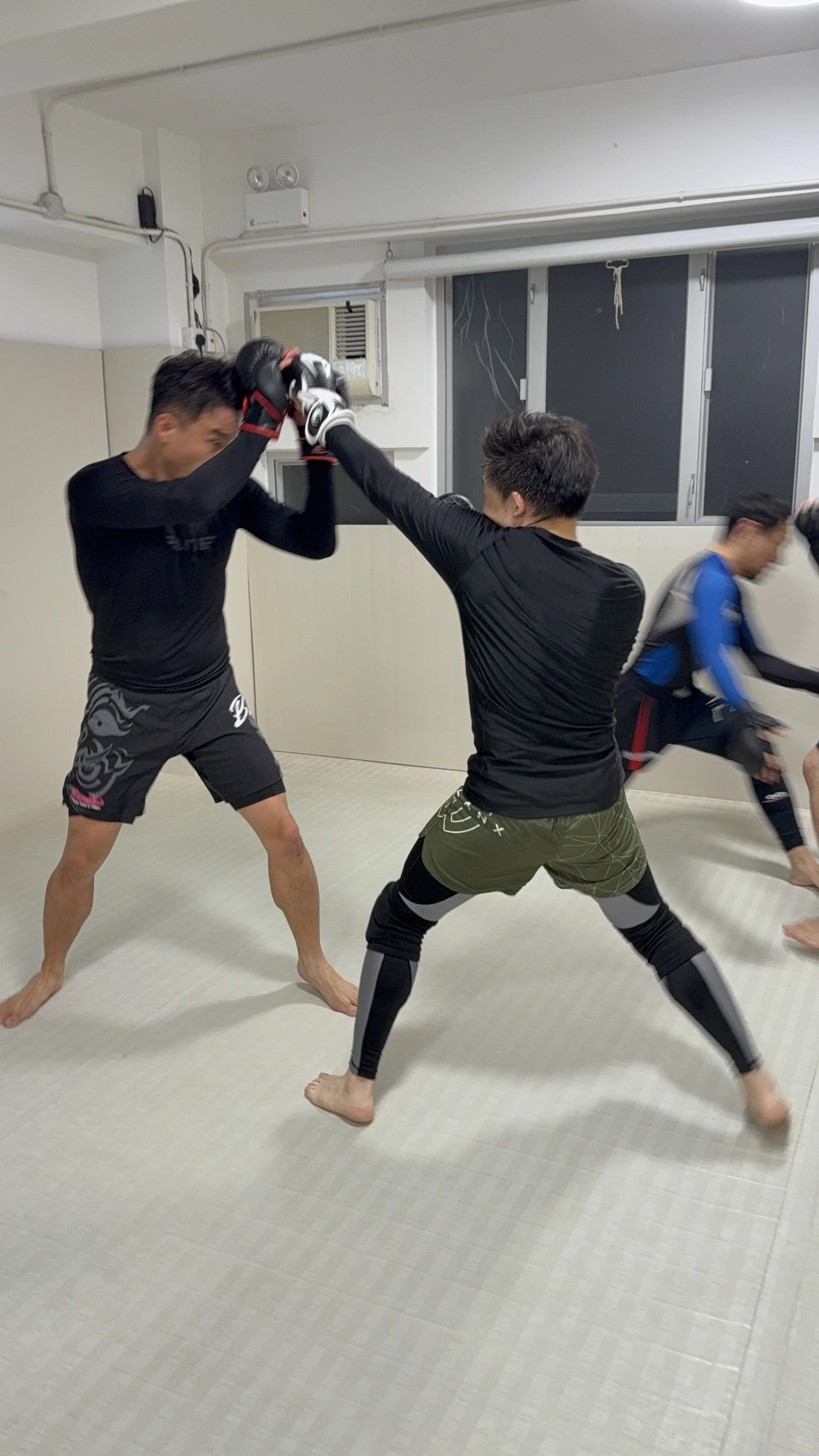 Two men sparring in a martial arts training session, practicing striking techniques, with a third man in the background