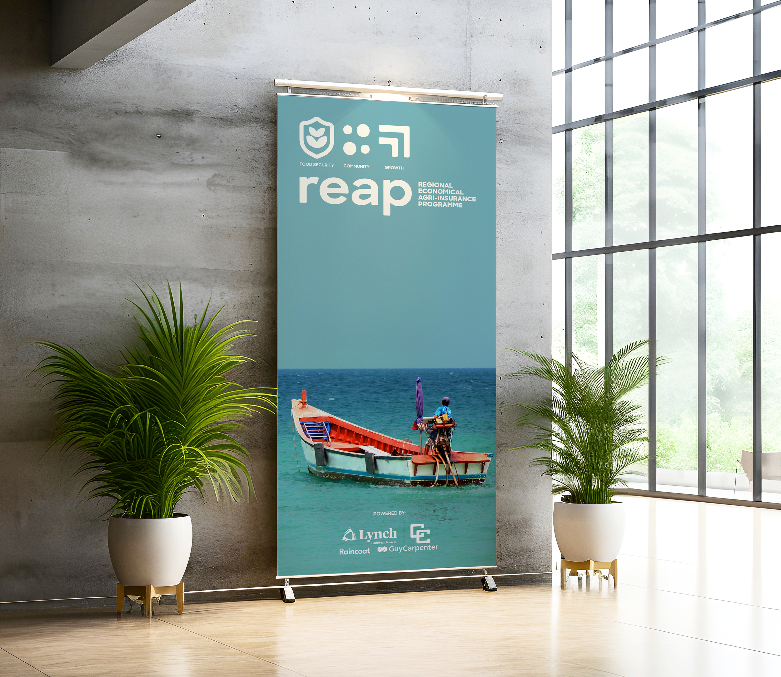 Indoor scene with a vertical banner on a concrete wall, featuring an image of a boat and people on the water, and text about a regional agricultural insurance program. Two potted plants are on either side of the banner.
