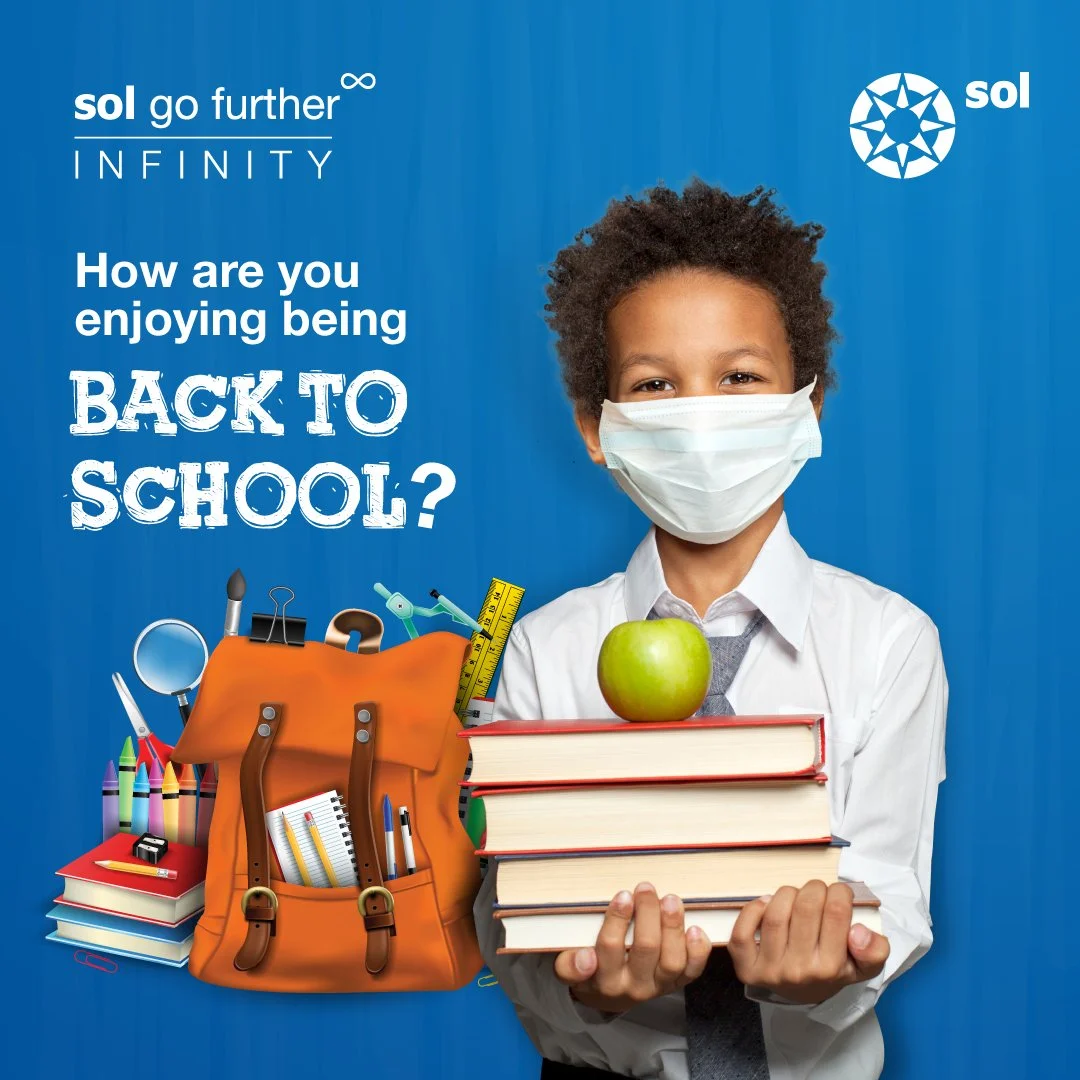 A young boy wearing a face mask, holding a stack of books with an apple on top, with school supplies and a backpack beside him. The background is blue with text about back-to-school.