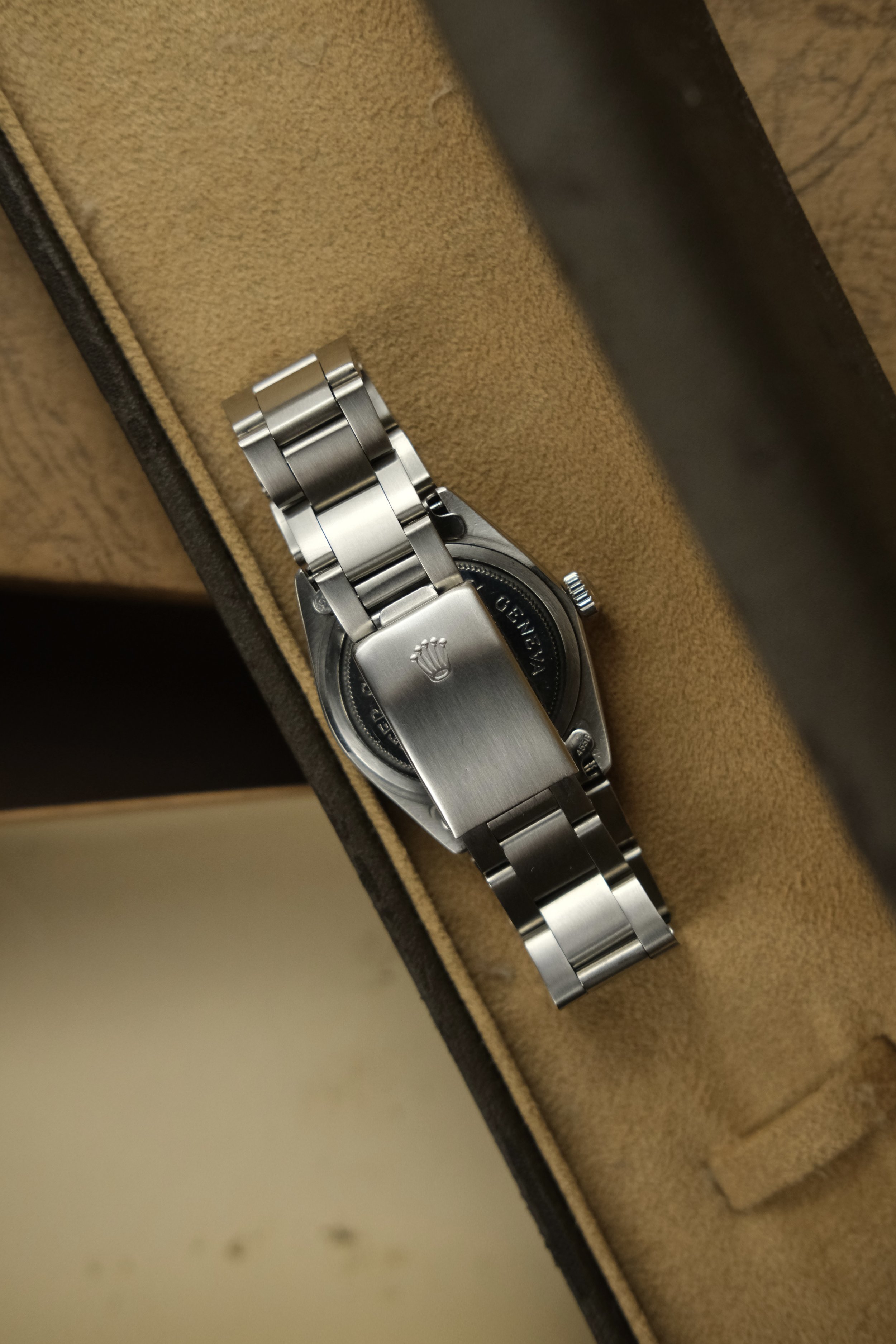 A stainless steel Rolex watch with a metal bracelet inside a tan watch box.