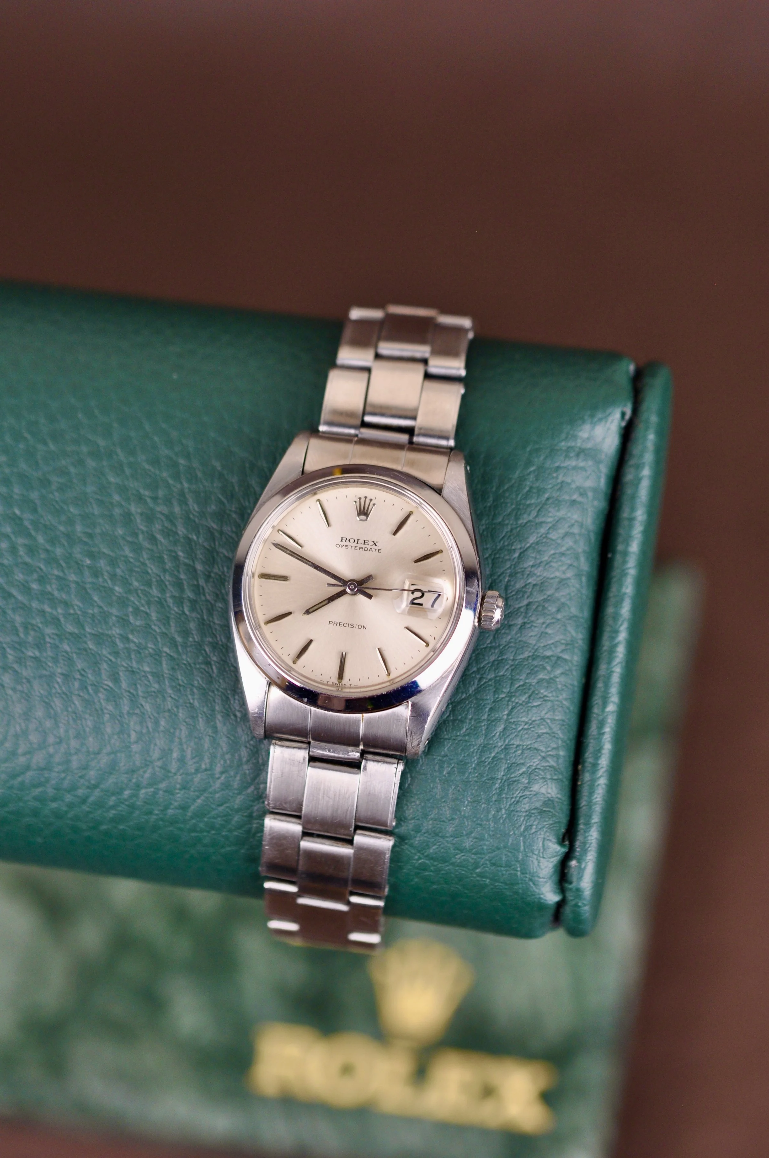 A vintage Rolex Oysterdate Precision wristwatch with a stainless steel band, cream dial, and date window, resting on a green Rolex box.