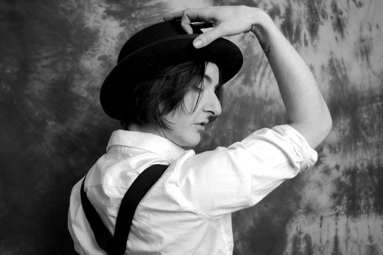 Femme en noir et blanc portant un chapeau noir, robe blanche à manches longues, regardant vers la gauche, fond texturé