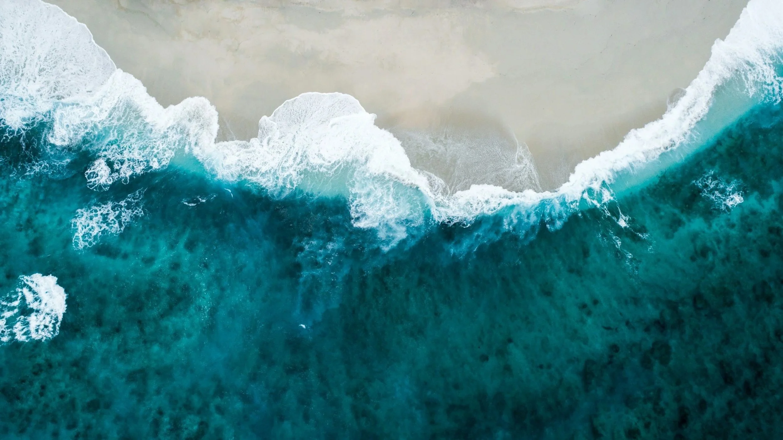 Aerial view of the ocean with large waves crashing onto a sandy beach