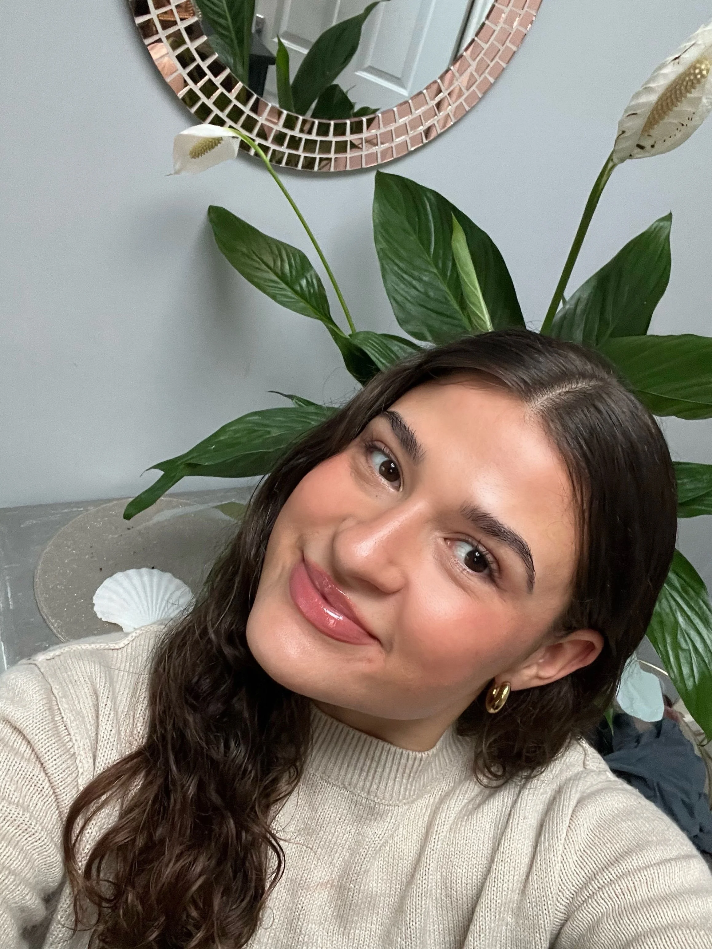Lily Horn, founder of The Peace Lily Practice, smiling in a cream jumper beside a peace lily plant.