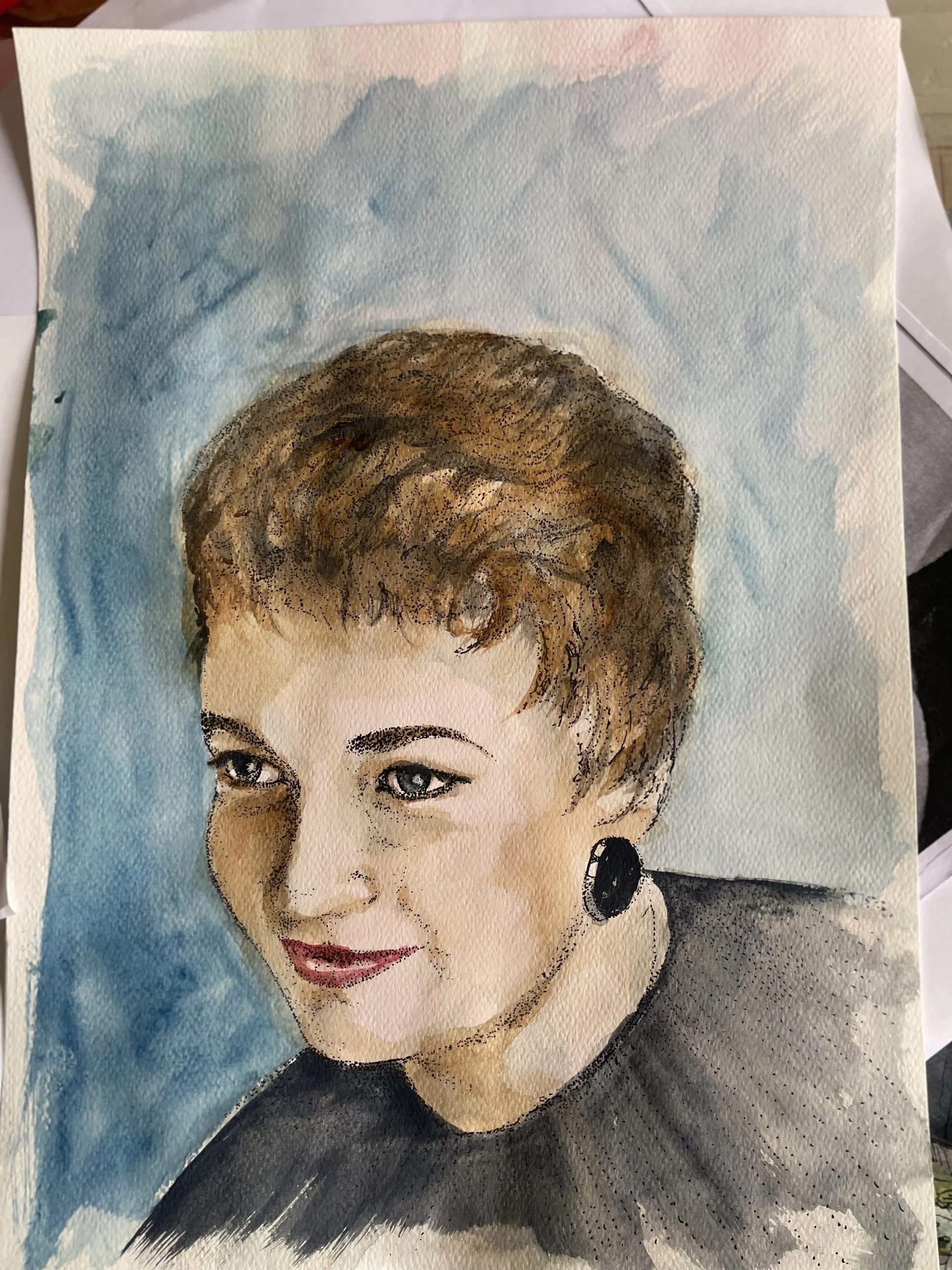 Watercolor portrait of a woman with short brown hair, wearing earrings and a black top, smiling with blue eyes and light skin.