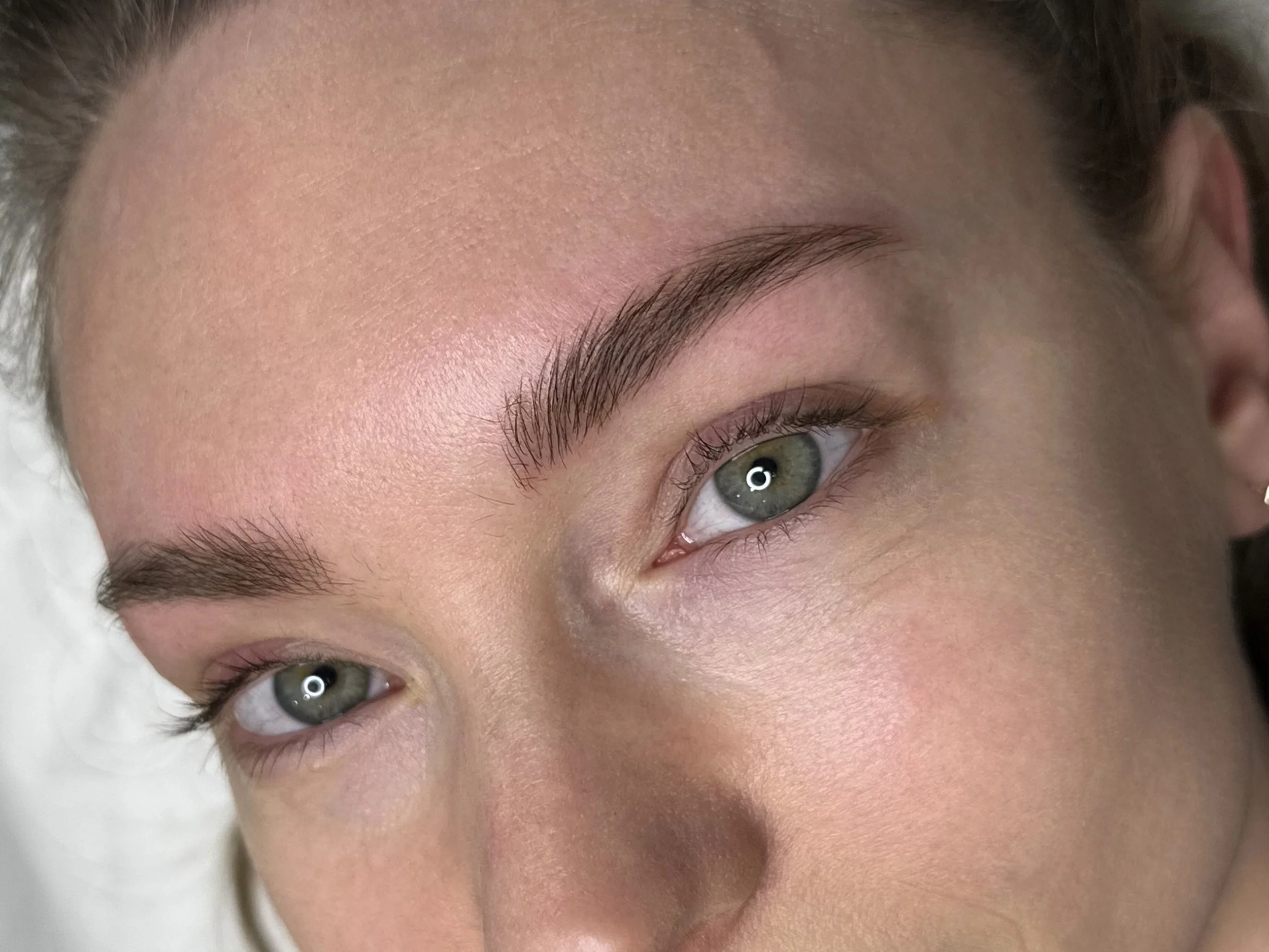 Close-up of a woman's face with well-groomed eyebrows, green eyes, and smooth skin.