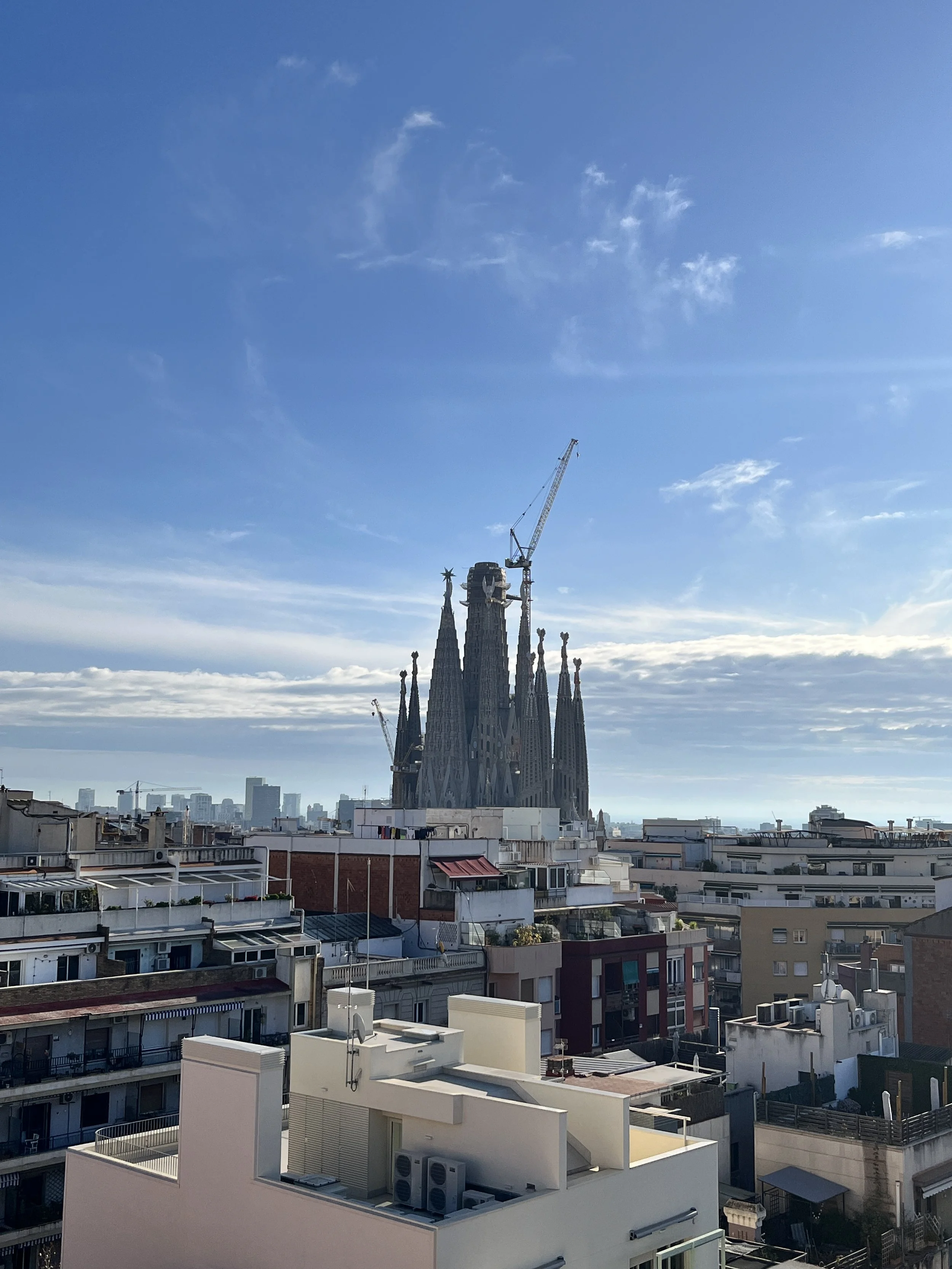 Vista de la Sagrada Familia en Barcelona, con edificios residenciales en primer plano y cielo azul con algunas nubes.