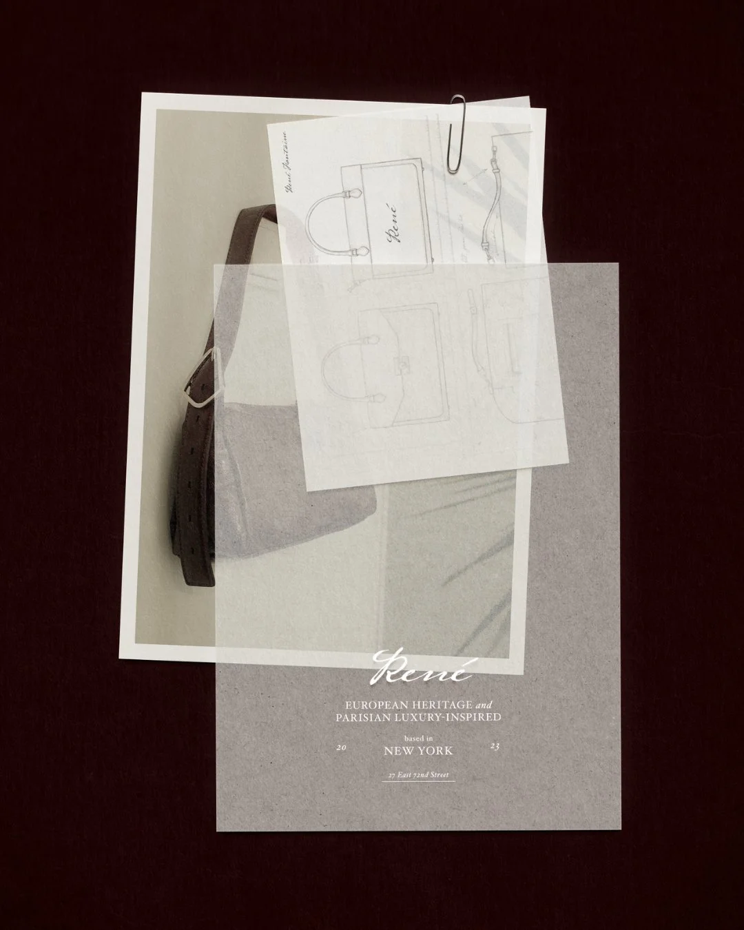 A table with a dark surface holding a printed sheet of paper, a sketch drawing of headphones, and a paperclip. The printed sheet advertises European heritage and Parisian luxury, referencing New York.
