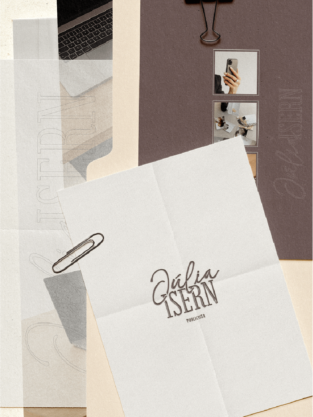 A white paper with the name Júlia Isern, Publicist, written in black; a paperclip attached to the paper; a dark purple notebook with the name Júlia Isern embossed on the cover; a mirror and small photographs on a brown surface.
