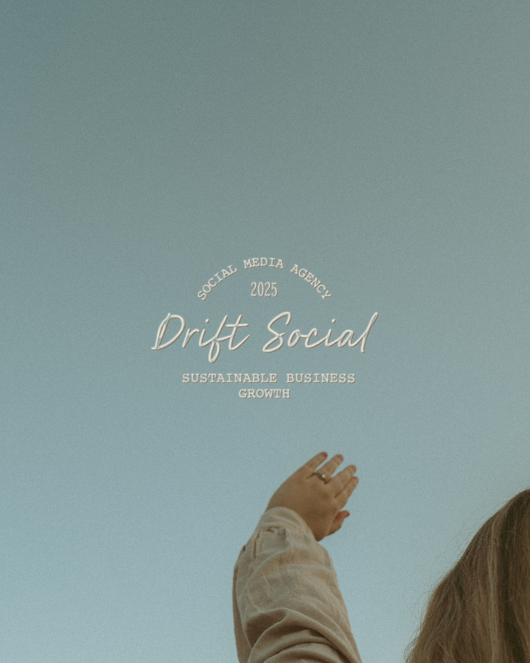A person in a beige shirt is reaching upward with their left hand, which has a ring on the index finger, against a clear blue sky. Overlayed text reads "Social Media Agency 2025 Drift Social Sustainable Business Growth."