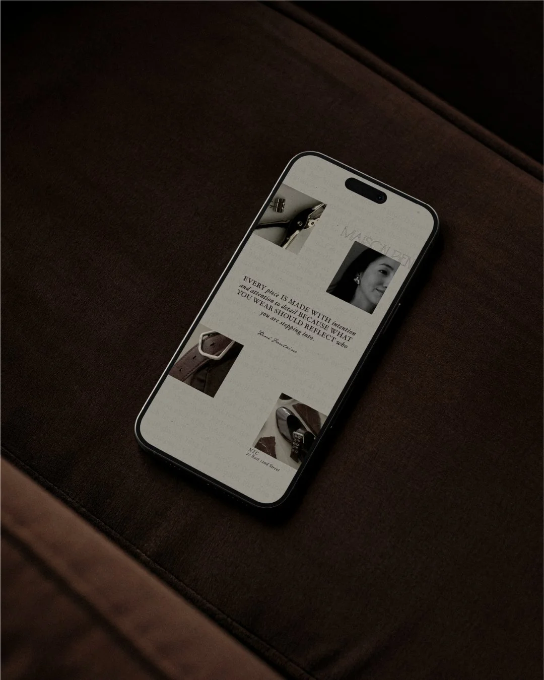 Smartphone resting on brown fabric surface displaying a webpage with black and white photos and text about craftsmanship and attention to detail.