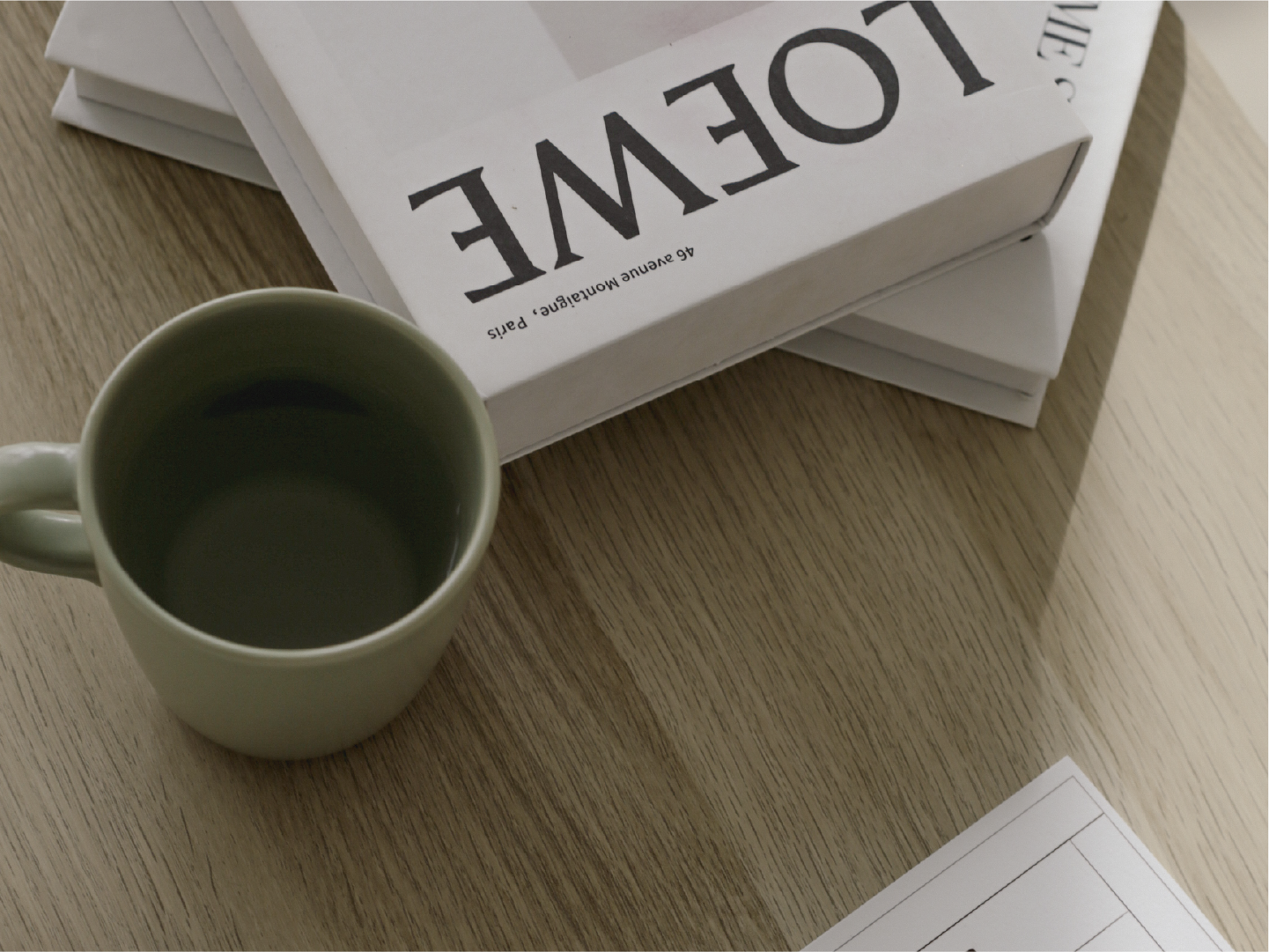 A white paperback book titled 'LOVE' with smaller text underneath, placed on top of another book, next to a white mug filled with a hot beverage, all on a light wooden table.