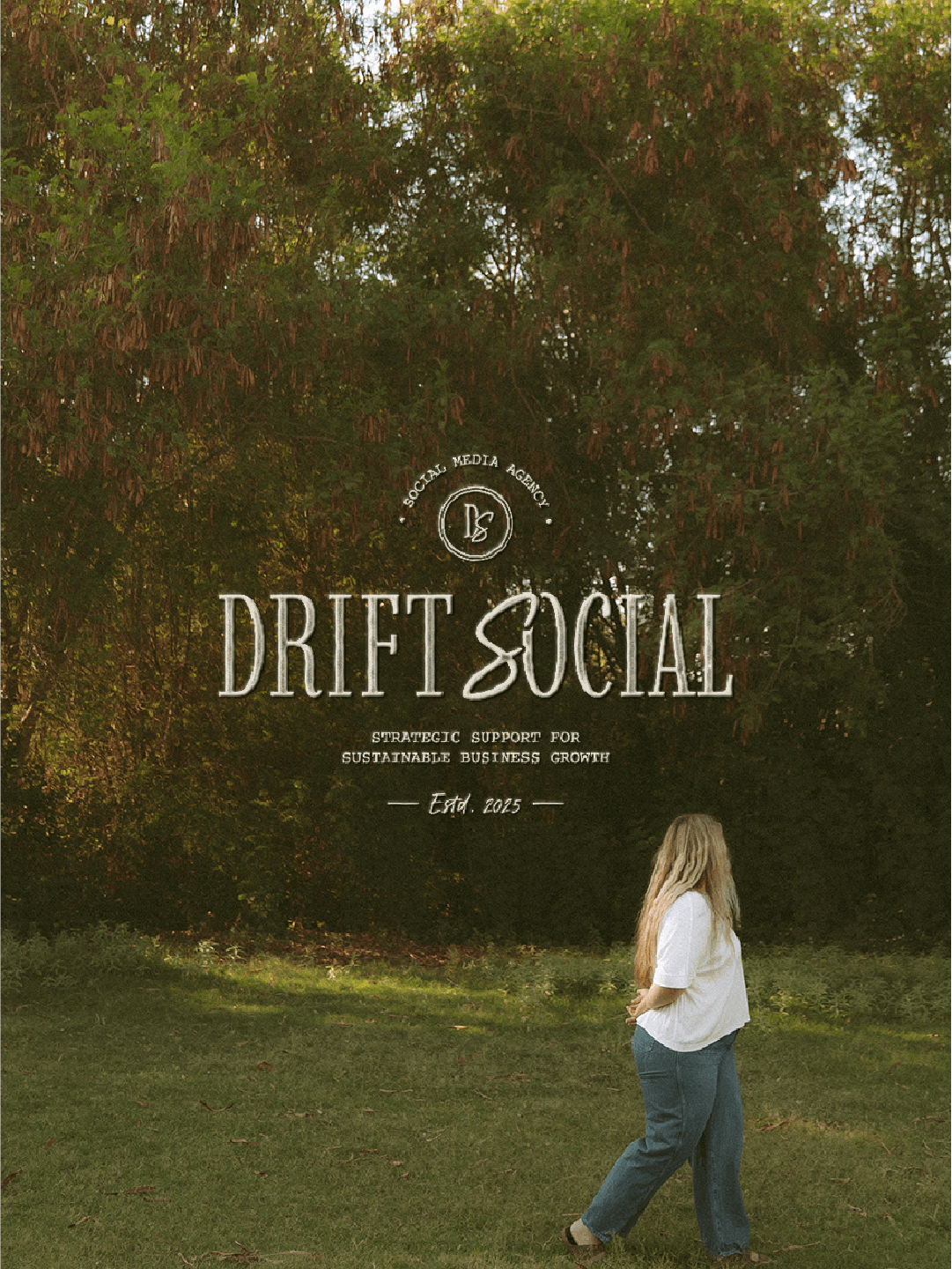 A woman with long blonde hair, wearing a white top and blue jeans, walking on green grass in front of dense trees with green and brown leaves. Overlaid text reads "Drift Social, Social Media Agency, Strategic Support for Sustainable Business Growth, Estd. 2025."