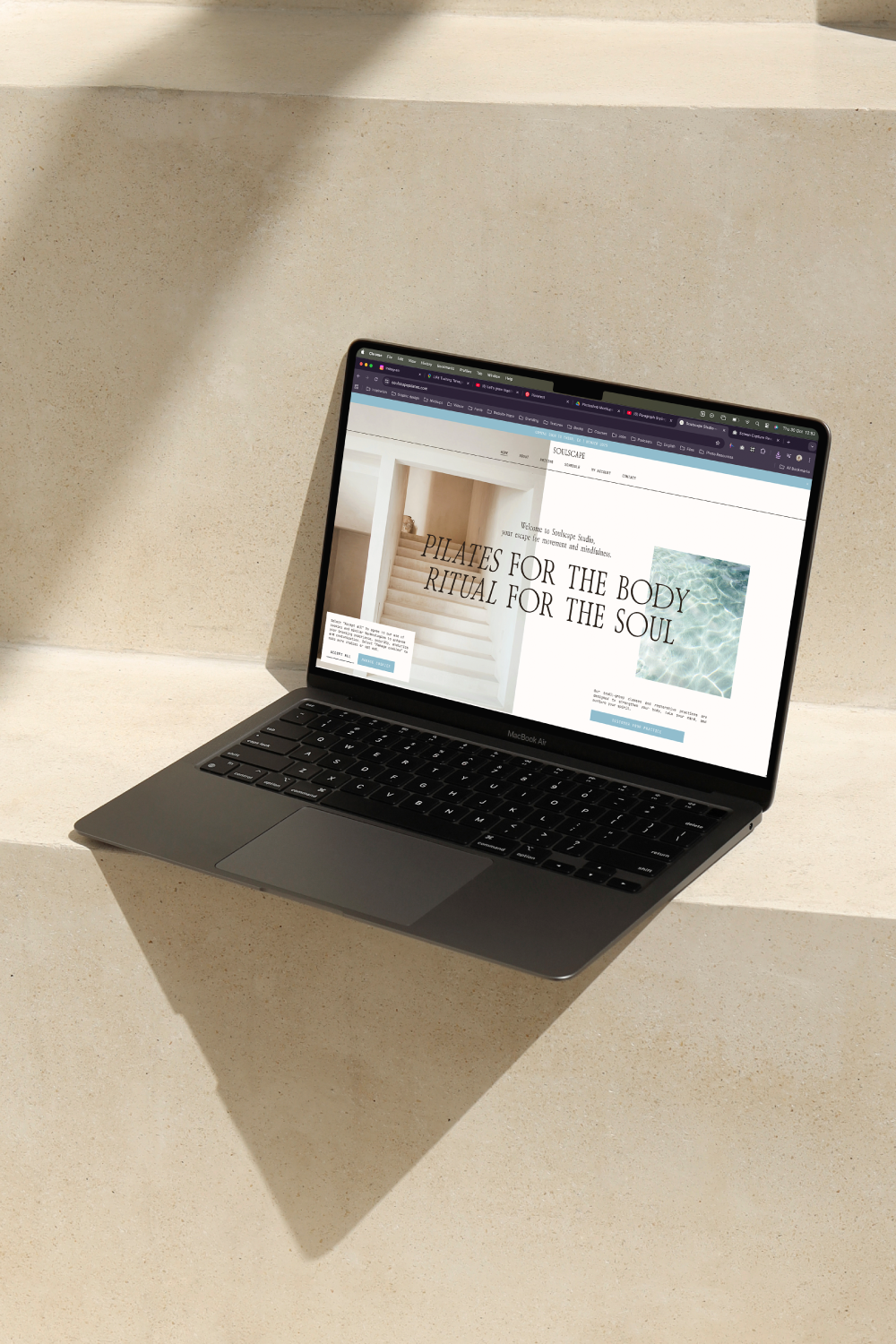 A MacBook Air on a beige concrete surface displaying a website about Pilates and wellness.