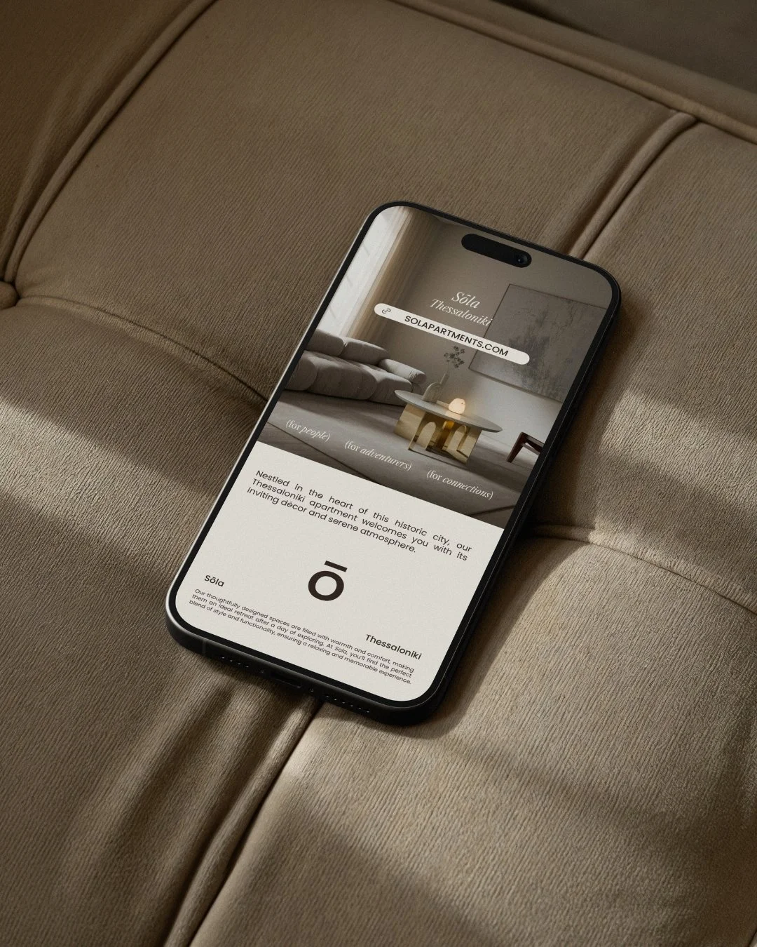 Smartphone displaying a website about Sola Thessaloniki apartments, resting on a beige fabric surface.