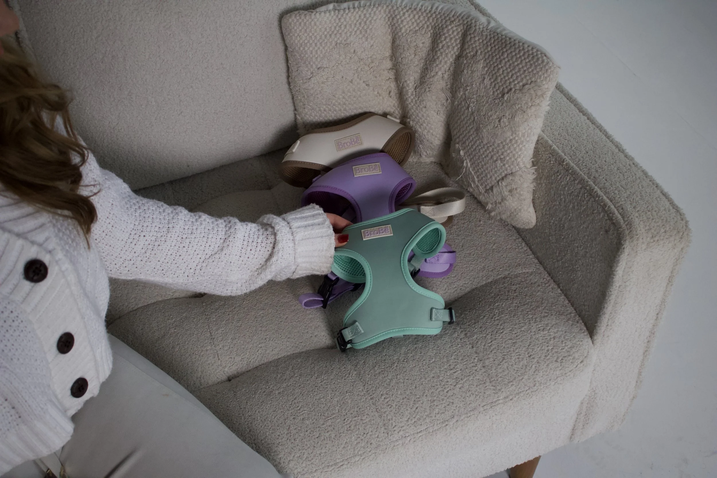 A woman arranging colorful braces and a beige pillow on a light beige textured couch.