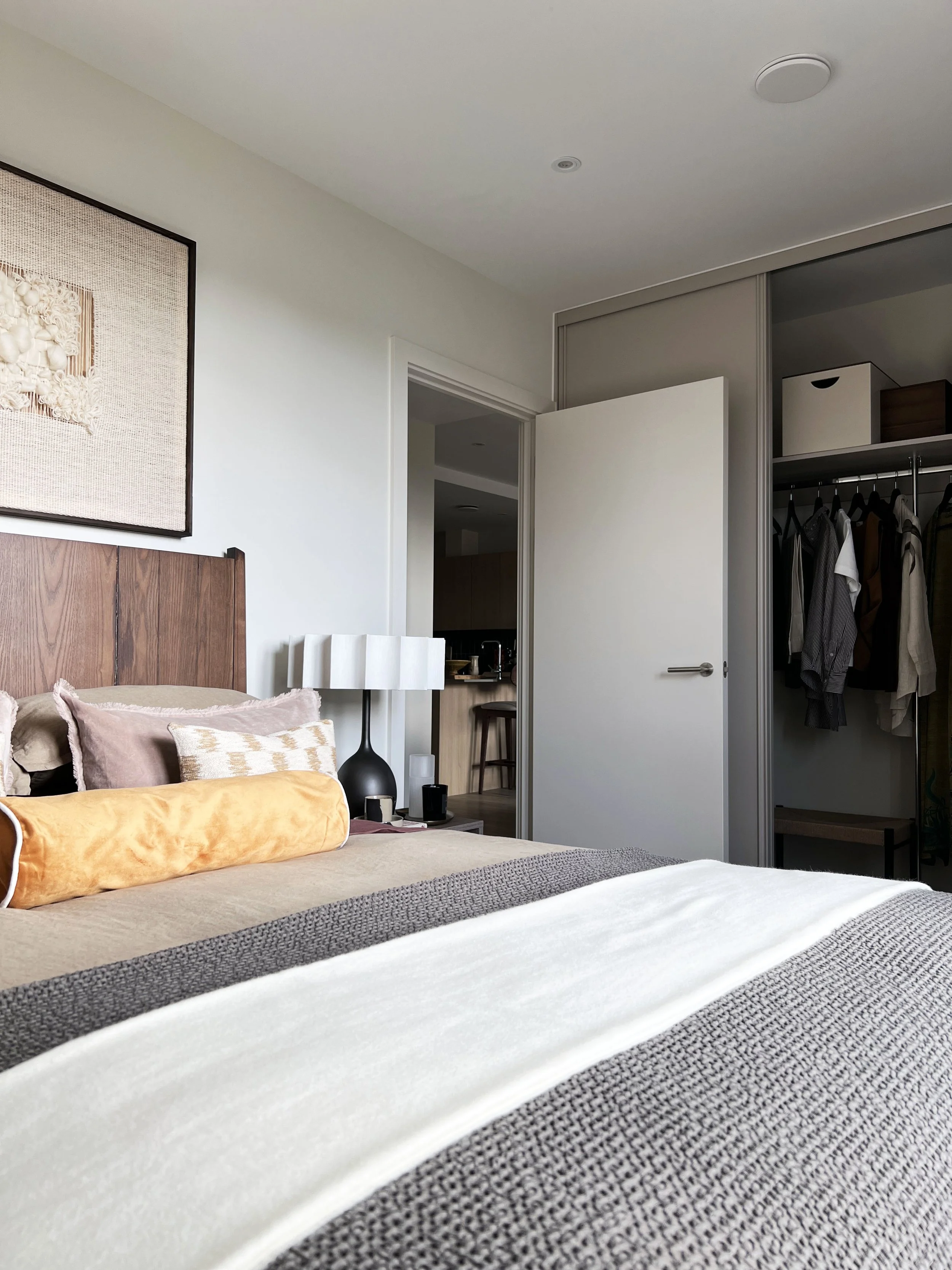 A neatly made bed topped with a throw and an orange bolster cushion.  