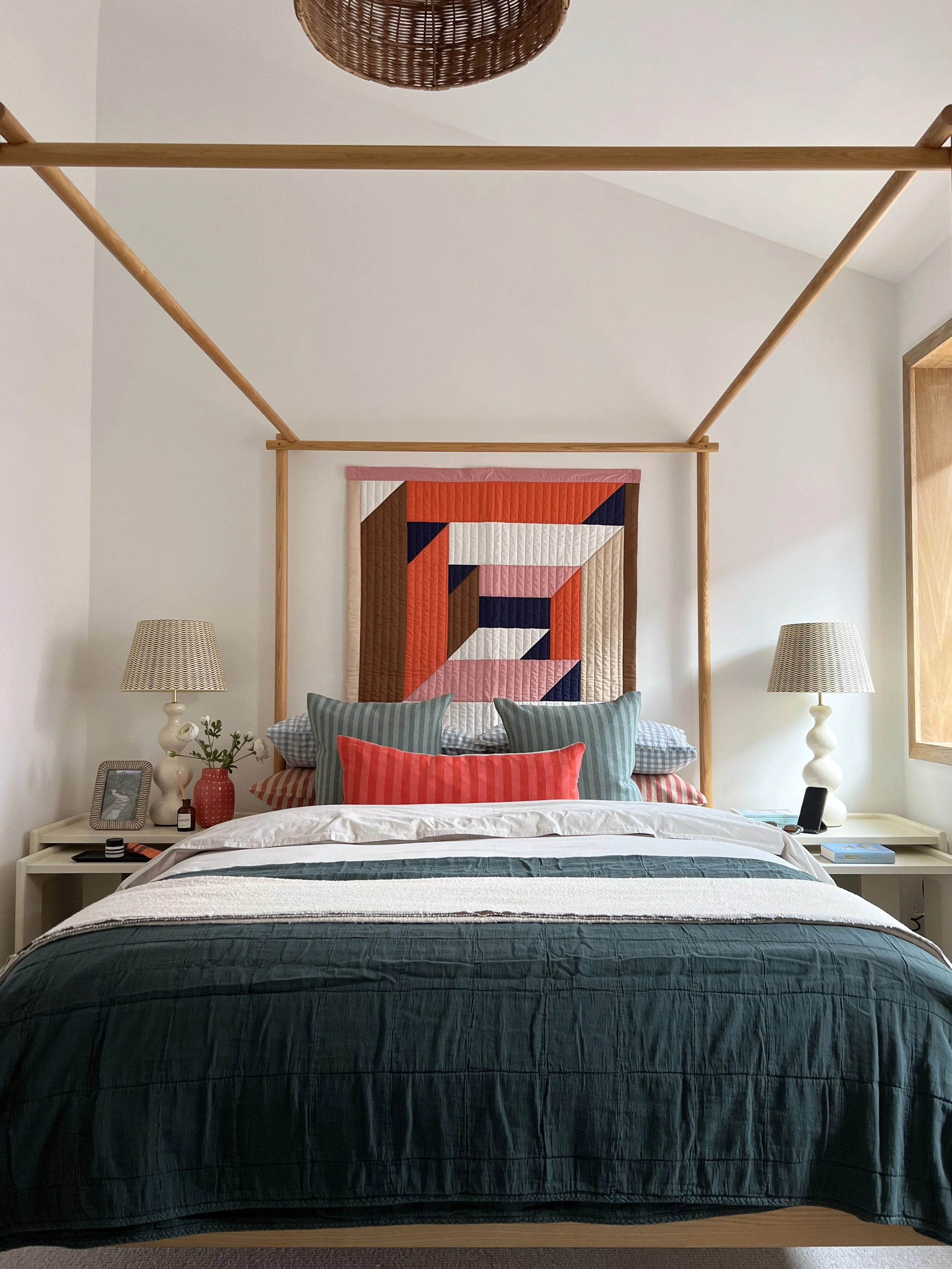 End view of a four poster bed in a bespoke show home, with large patterned fabric wall hanging