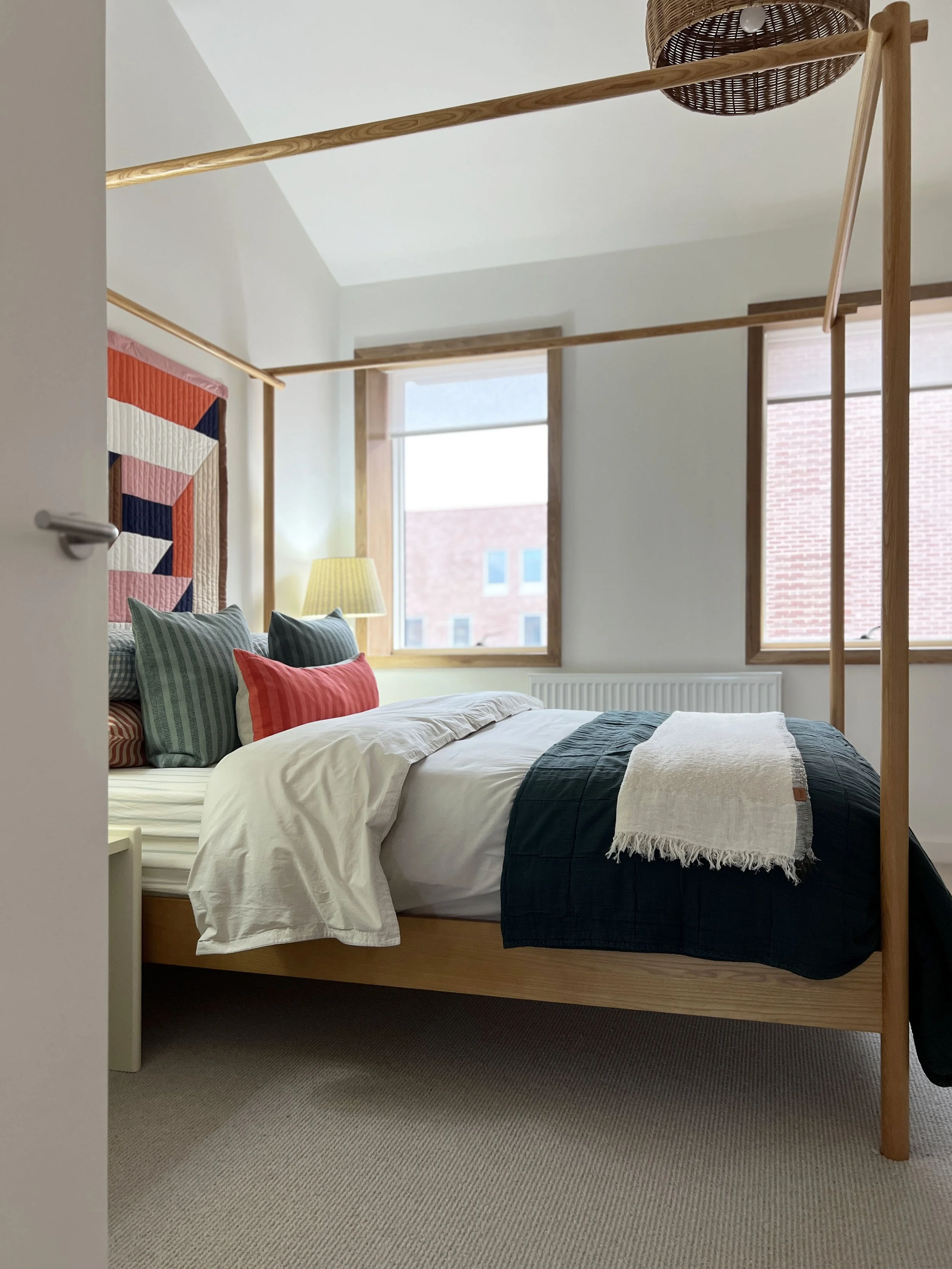 A fully dressed four poster bed with orange scatter cushion 