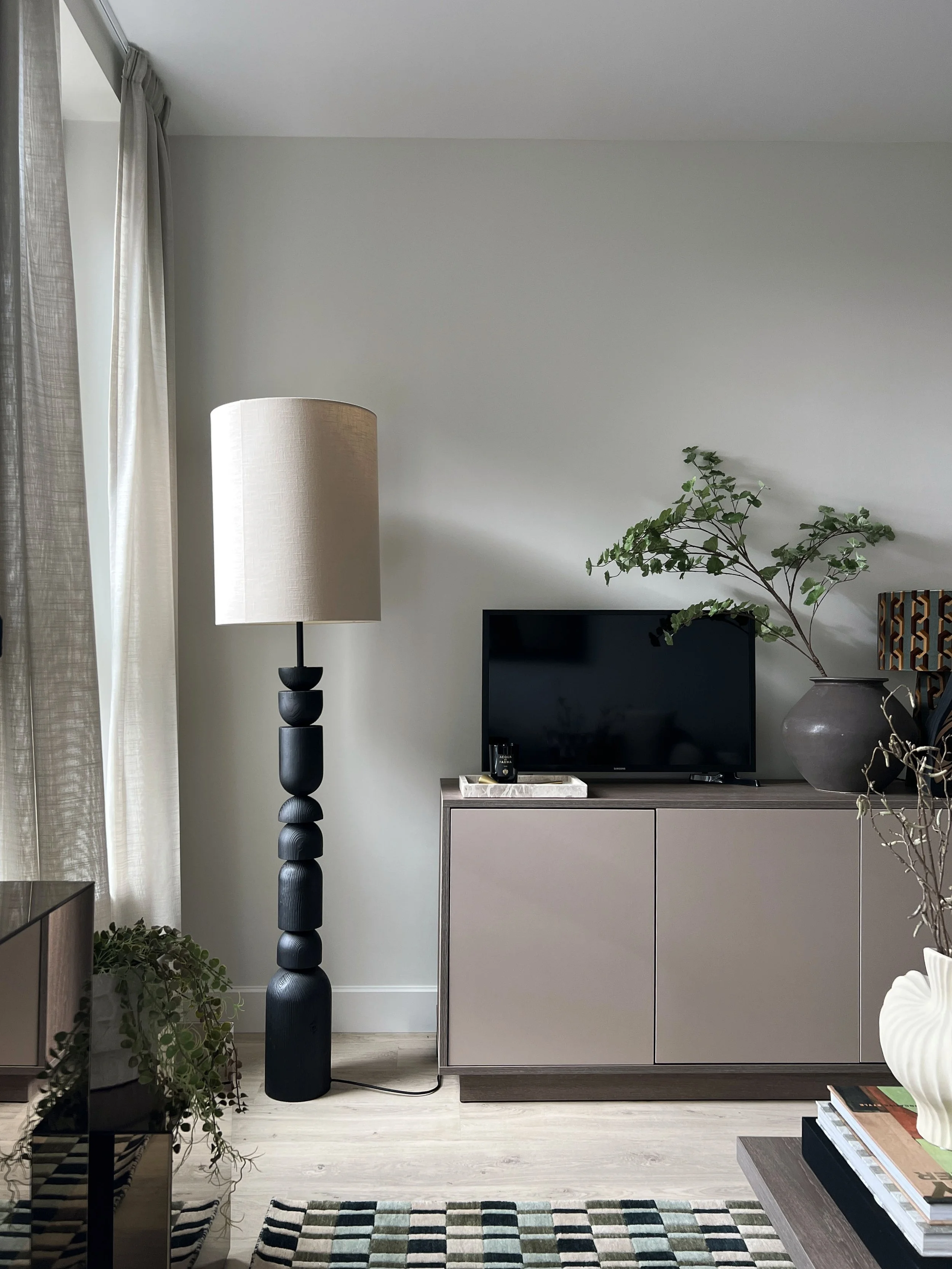 A tall textured lam with large cream lampshade, sitting aside a sideboard in a showhome living room