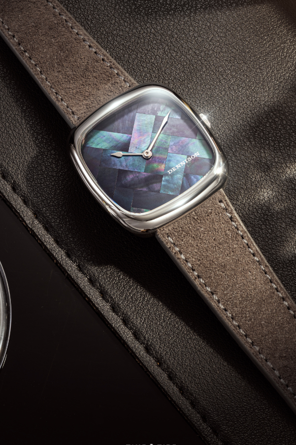 A Dennison x Time+tide Watches DateNight wristwatch with a square face displaying a Mother of Pearl pattern, placed on a brown leather strap and dark textured surface.