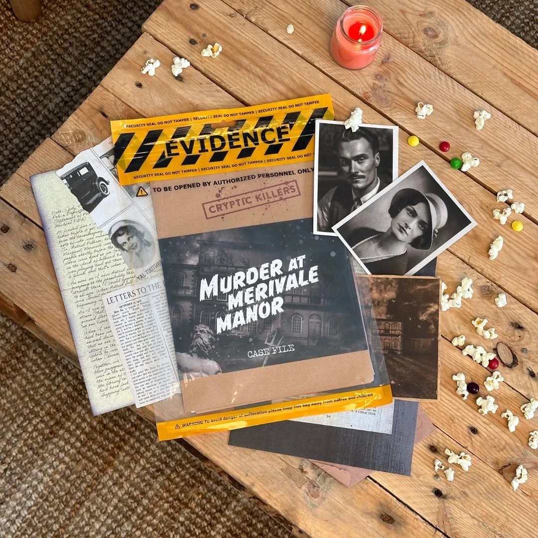 A wooden table with a lit pink candle, scattered popcorn, colorful candies, and various vintage-style papers and photographs, including a murder mystery case file and police tape labeled 'Evidence.'