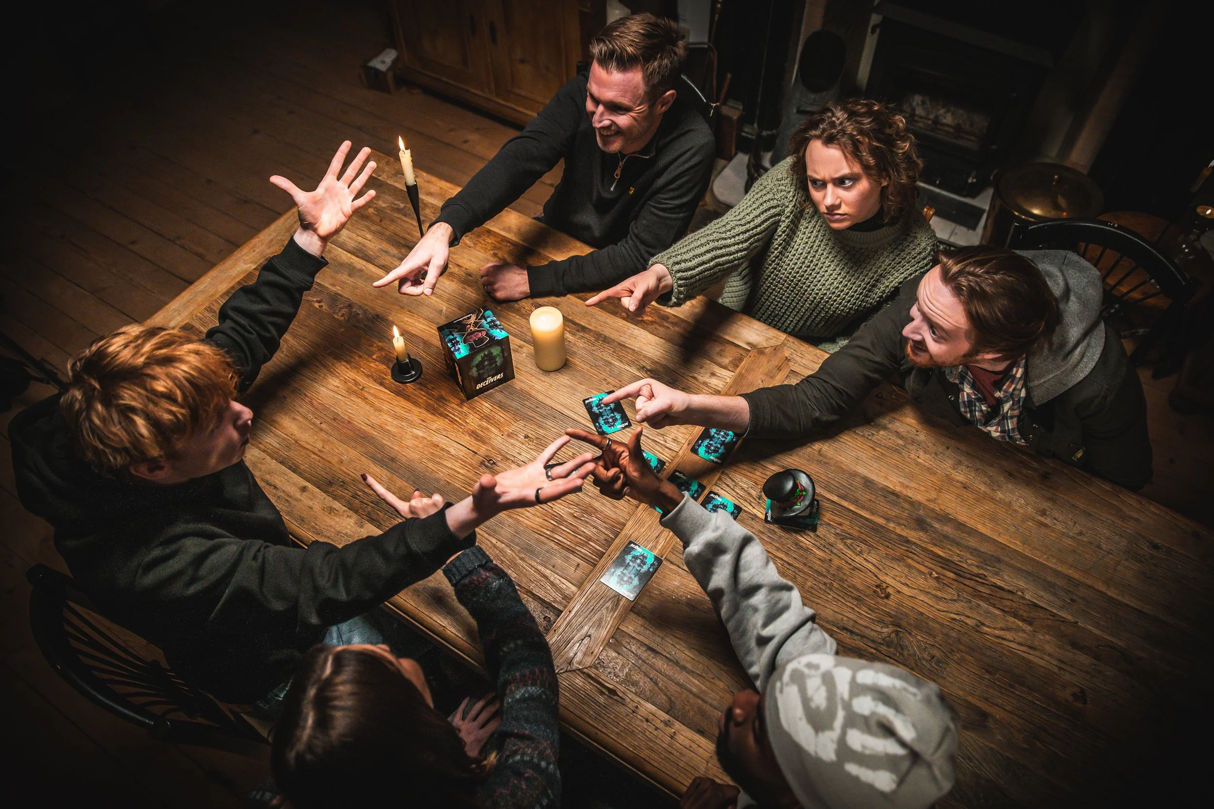 Group of six friends playing a tabletop game at a wooden table, with candles and game cards, in a cozy, dimly lit room.