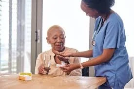Nurse administering medication to an elderly woman at a wooden table.