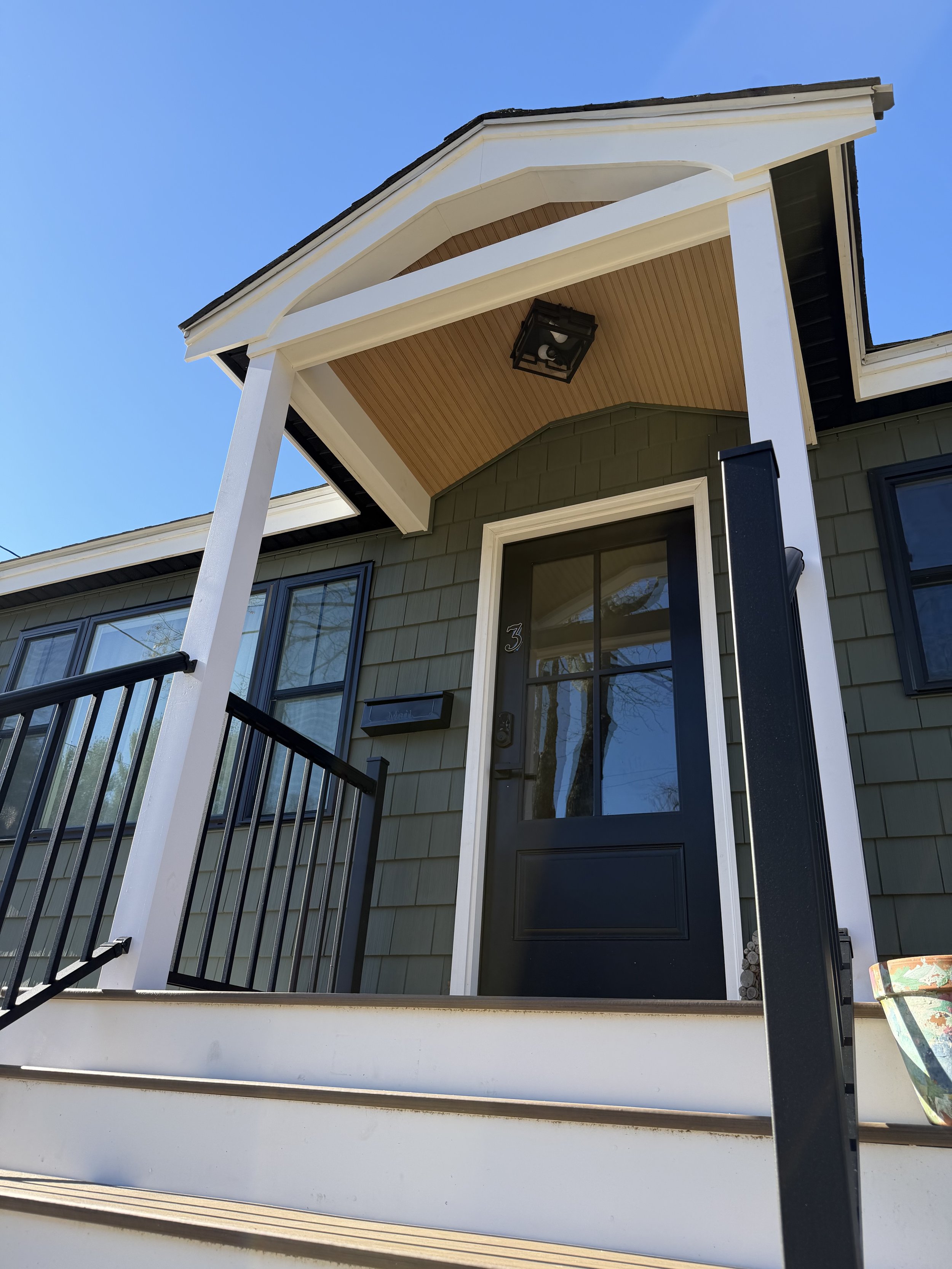 Close-up of a house front door with steps, black door, window, mailbox, and porch roof with light fixture.
