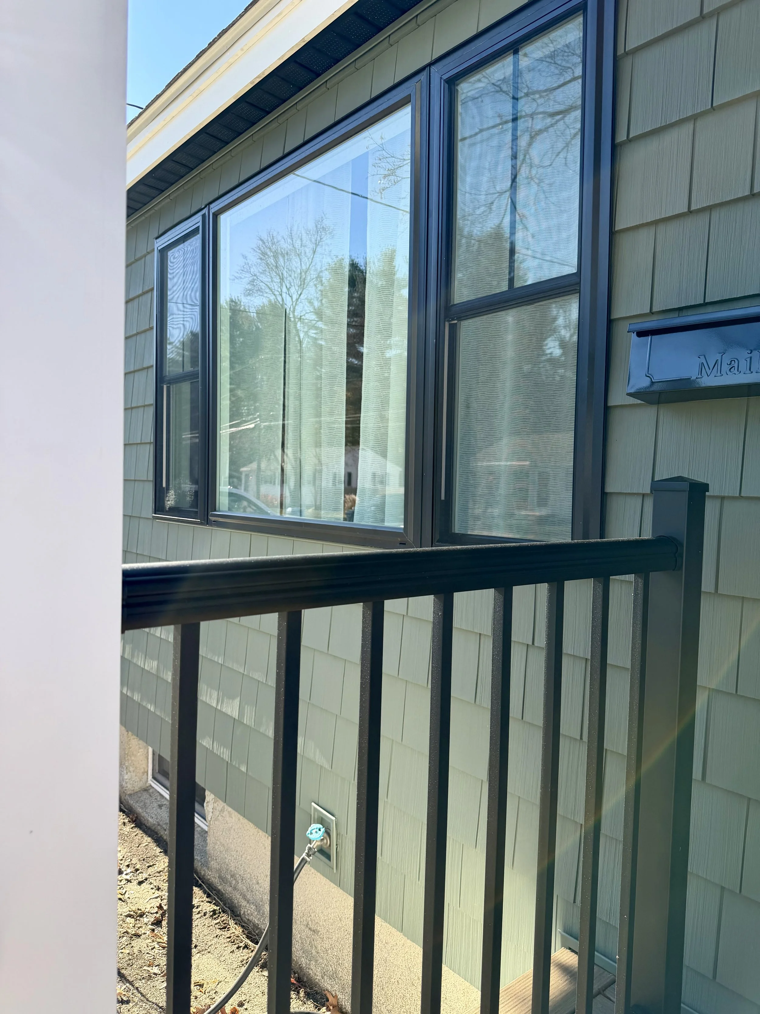 View of the side of a house with large window panes, a small black metal railing, and a blue mailbox on the wall.