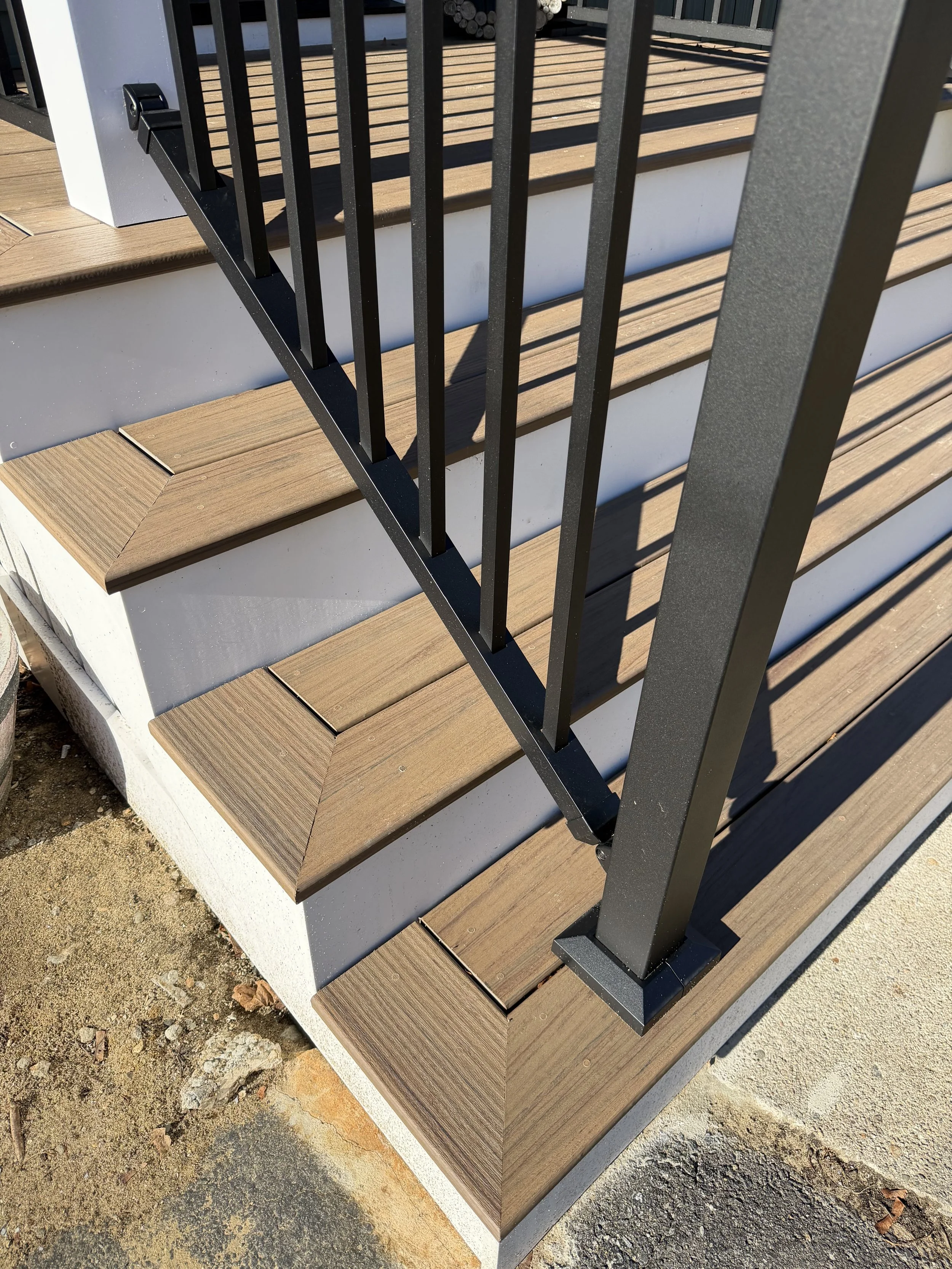 Close-up of outdoor wooden stairs with black metal railing and white foundation under the steps.