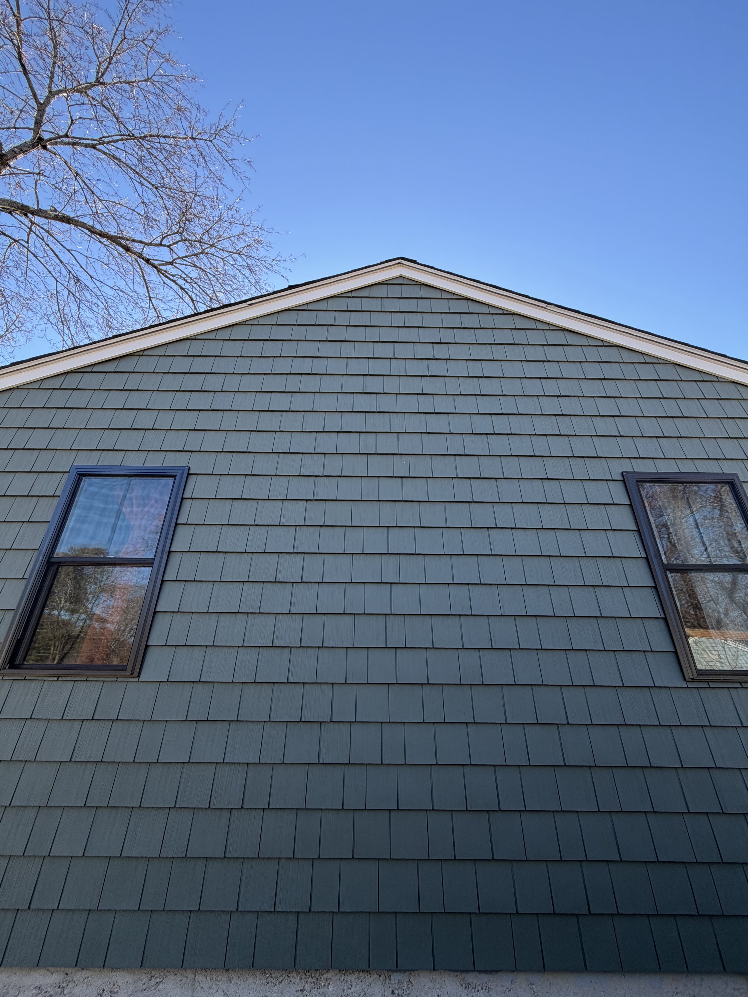 Close-up view of the exterior side of a house with blue shingles, two windows, and a clear blue sky in the background.