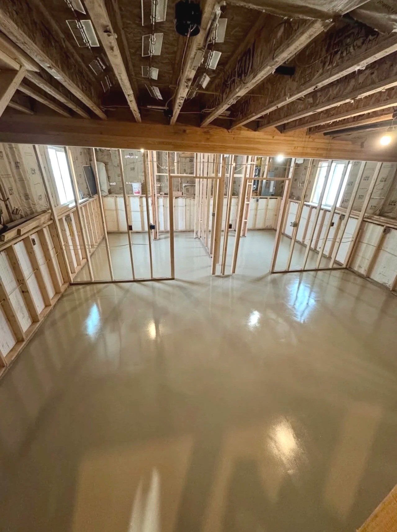 Interior of a house under construction with wooden framing, unfinished walls, and a freshly poured concrete floor.