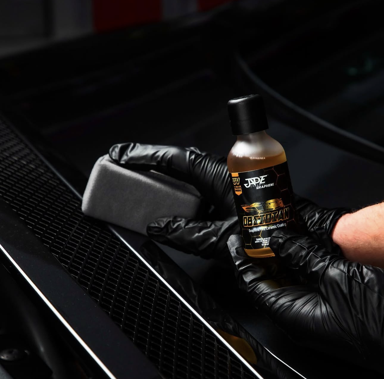 Detailer with black gloves on applying Jade Obsidian ceramic coating while holding it's bottle