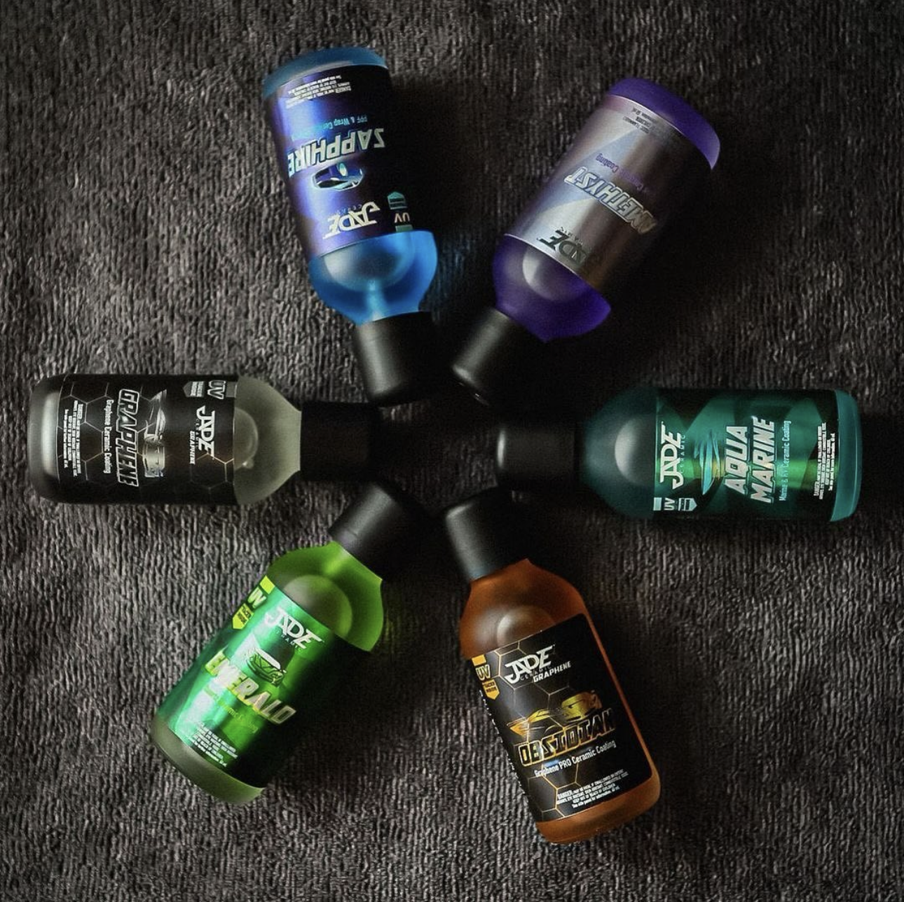 Six bottles of Jade ceramic coatings arranged in a circle on a dark textured surface.