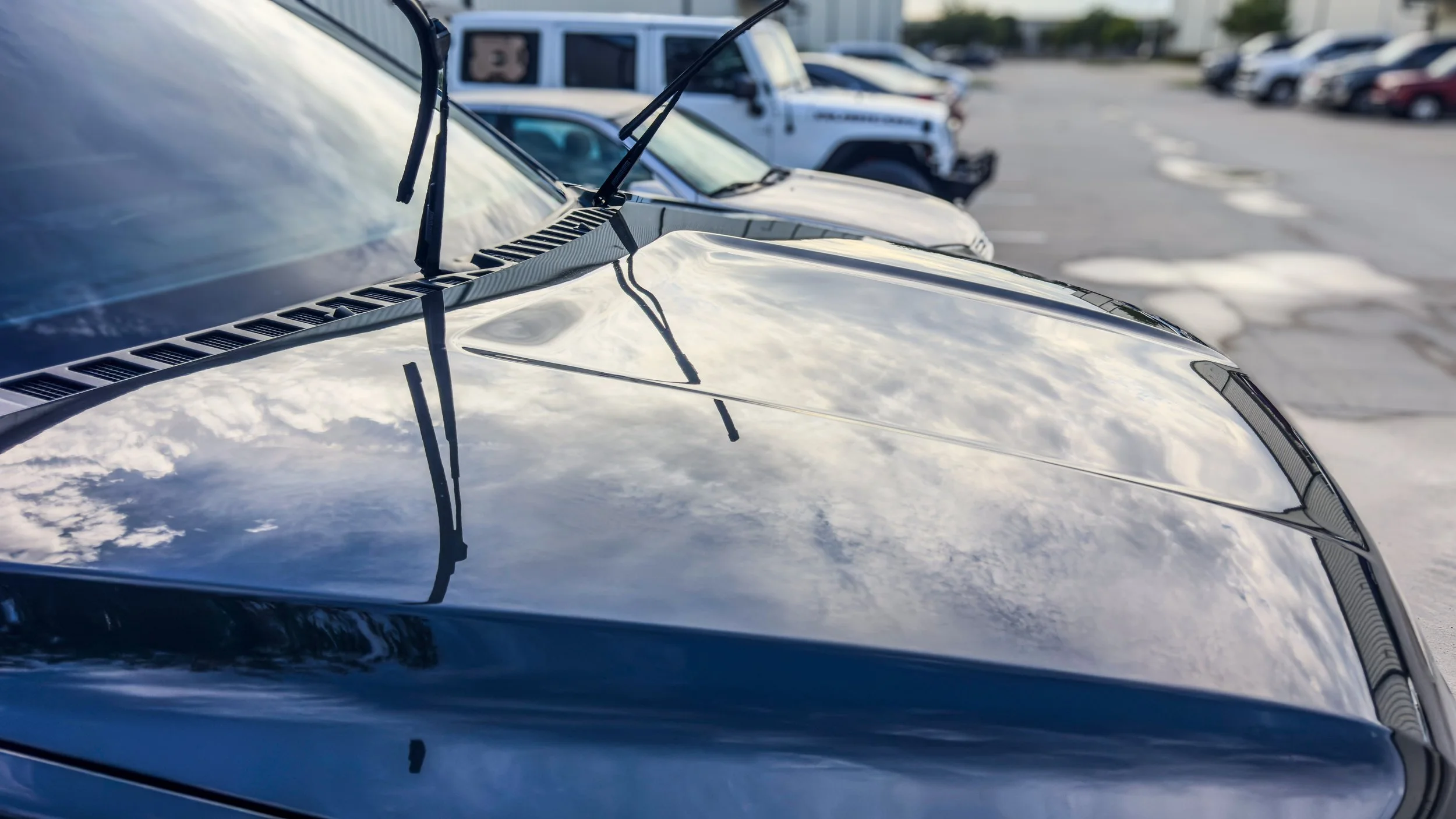 Close-up picture of a detailed car's hood showing the clarity by the mirror-like reflection of the sky seen on it.