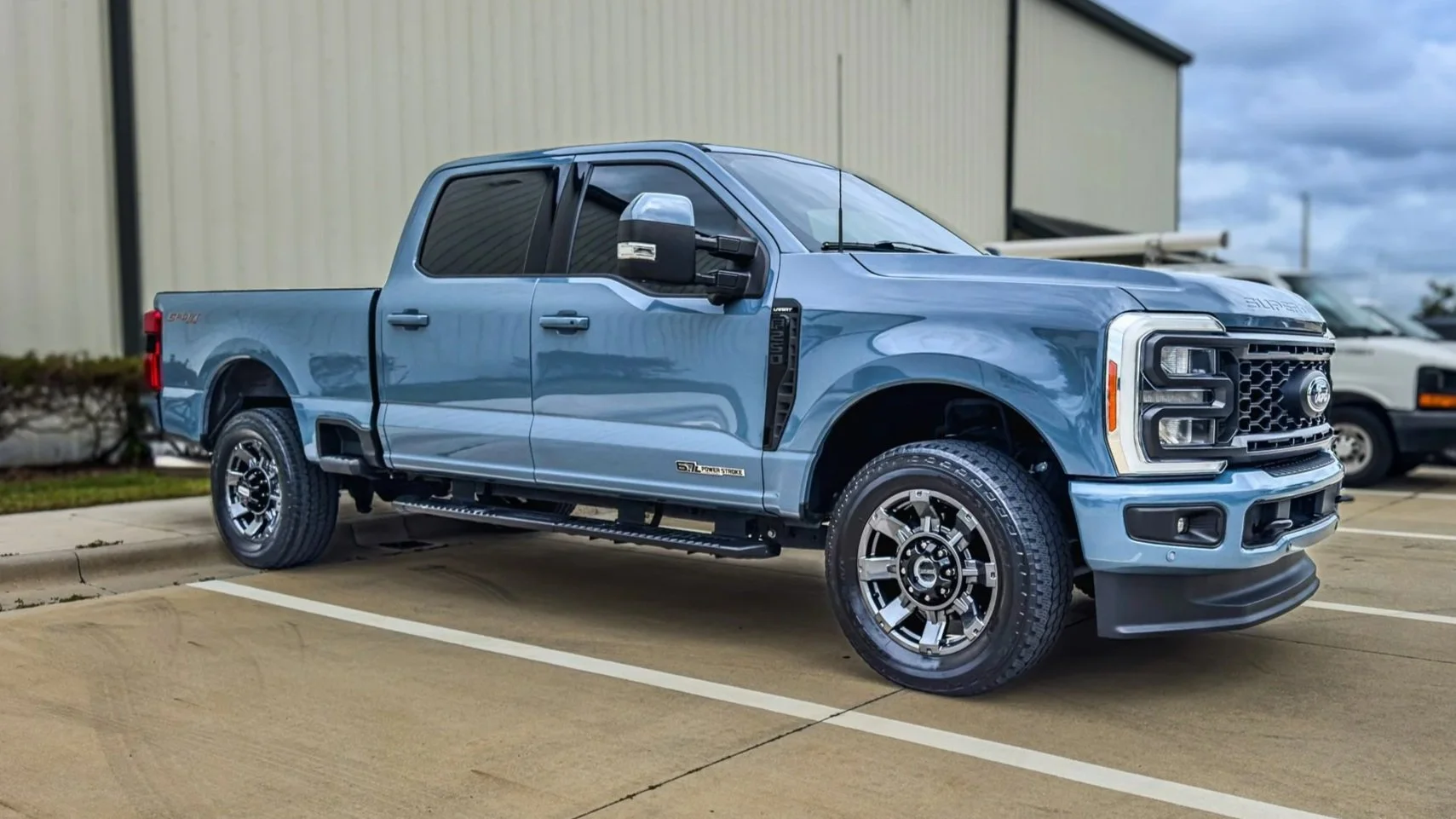 Blue Ford Super Duty pickup truck parked in a lot with a beige industrial building in the background.