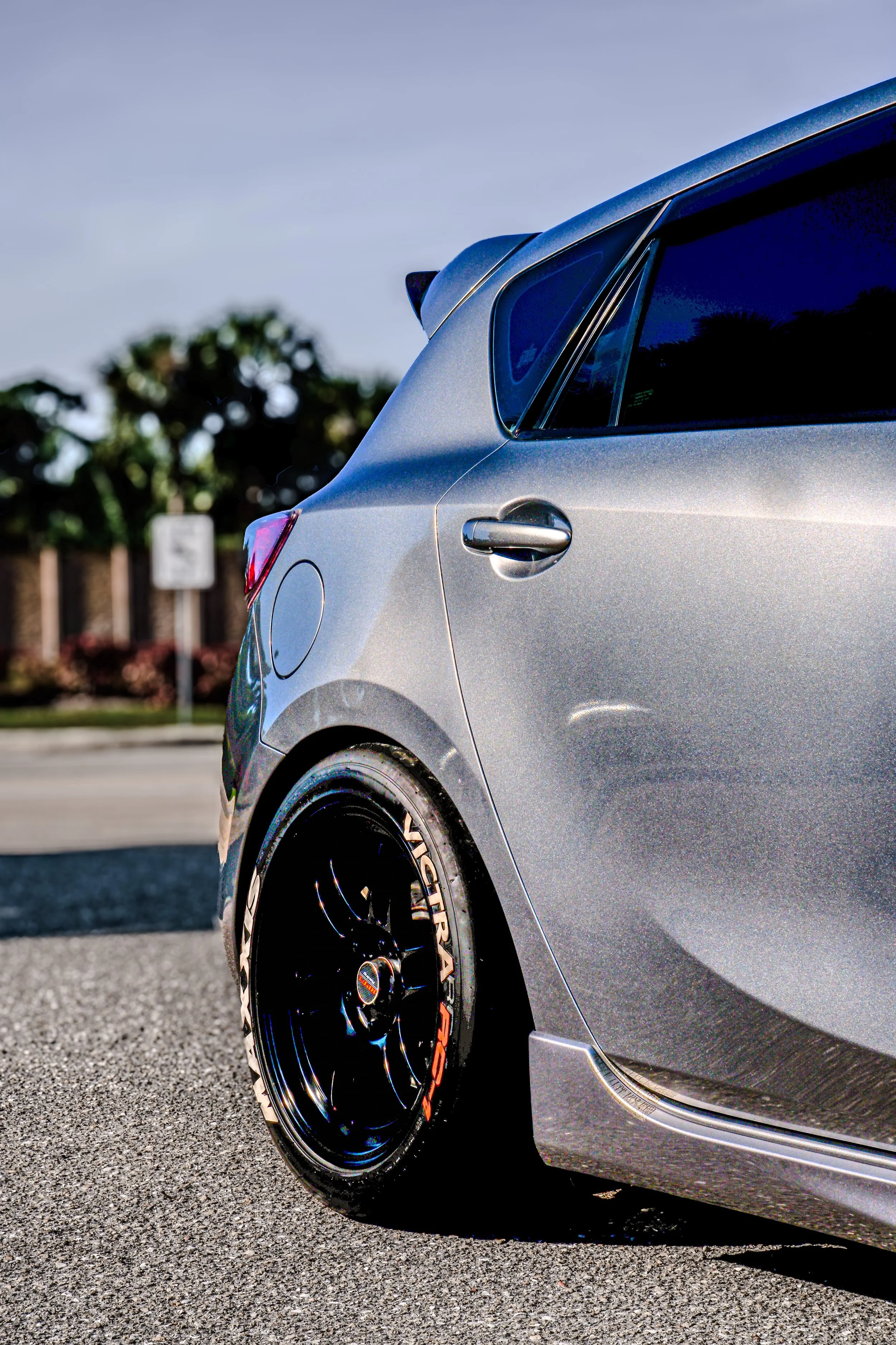 Close-up of the rear side of a silver hatchback car parked on the street with black wheels and tinted windows.