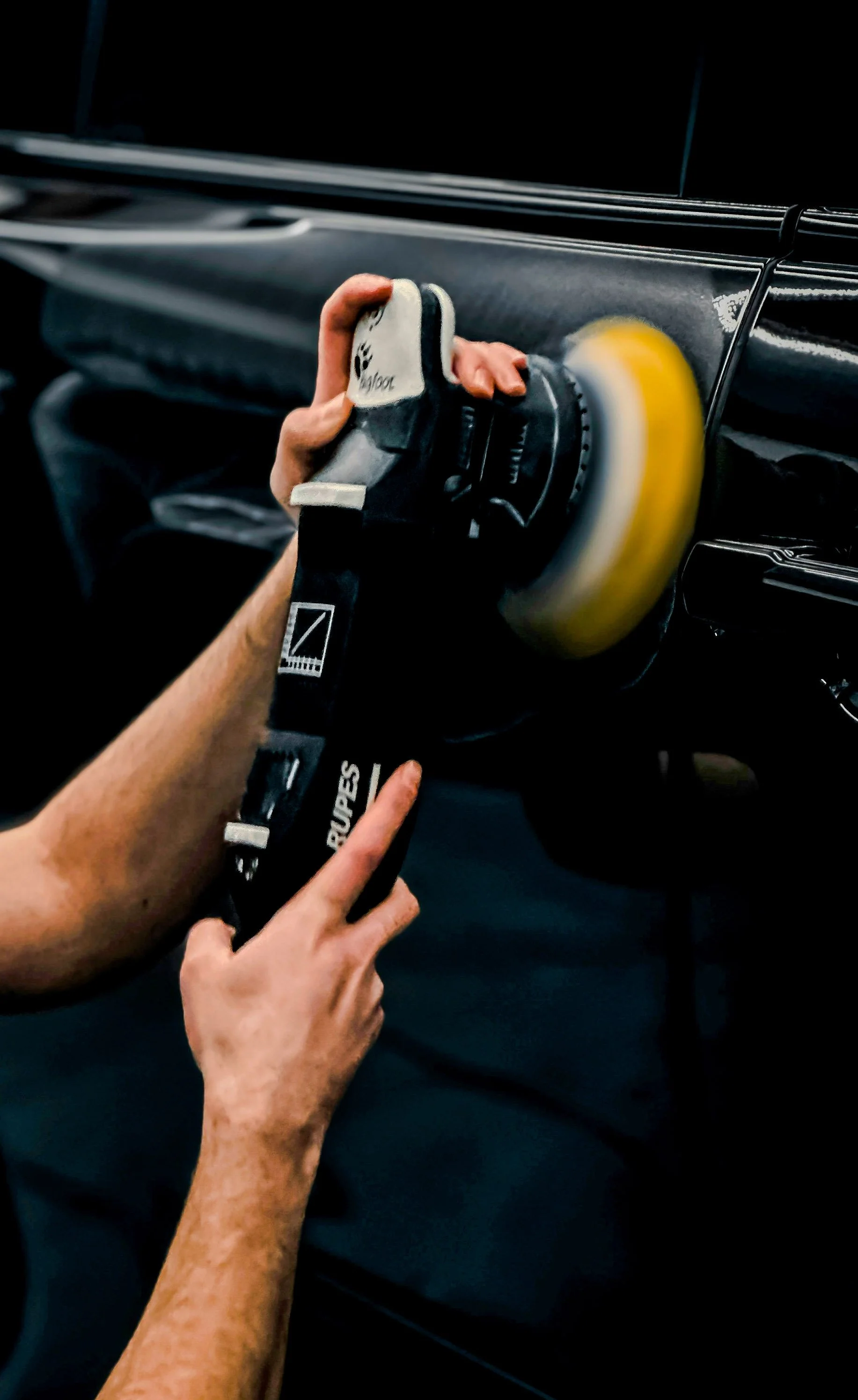Person polishing a black car with a dual action polisher.