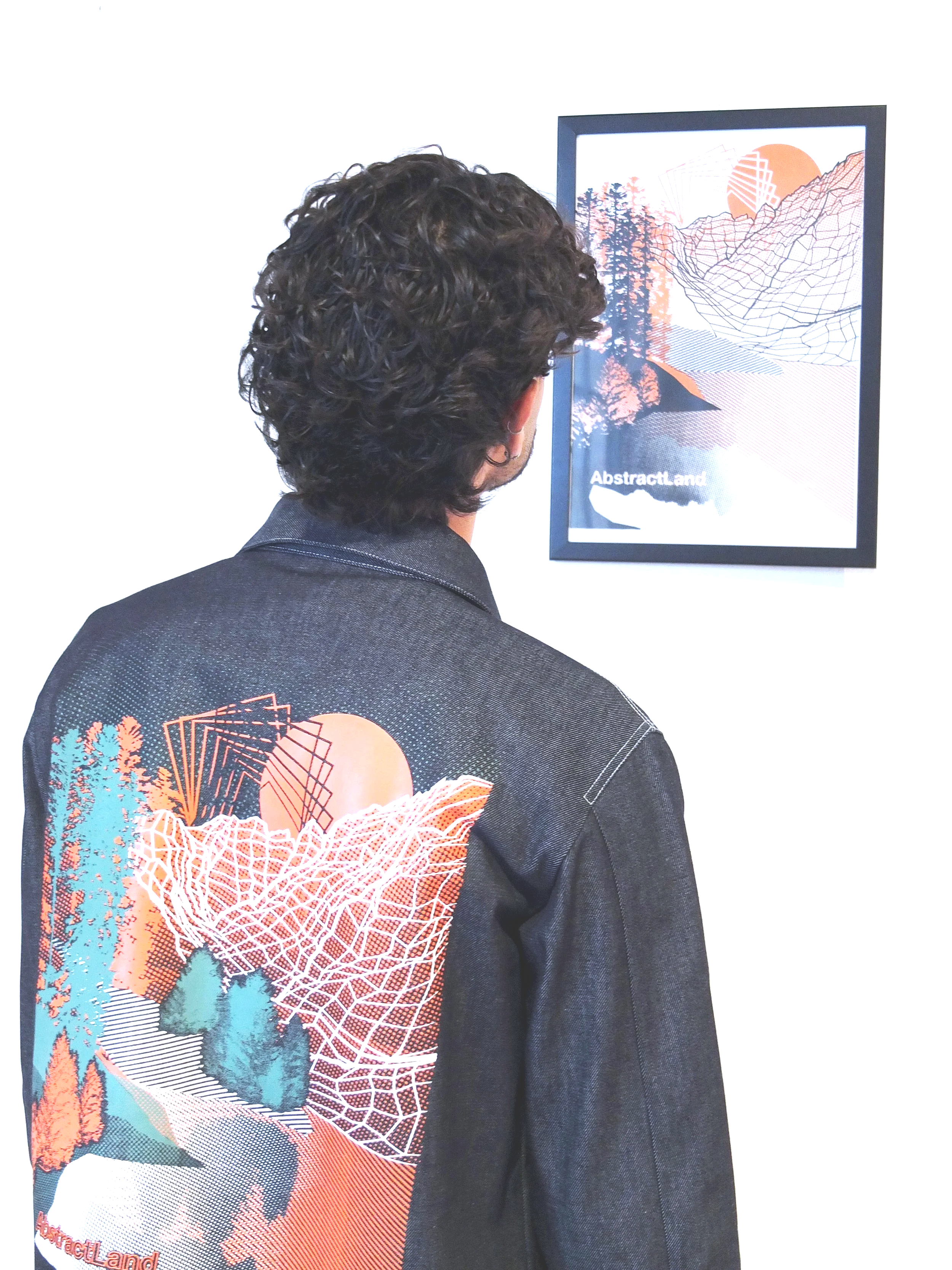 Un homme vu de dos est habillé avec une veste de travail en jean avec une sérigraphie sur le dos de la veste. Il regarde une œuvre d'art numérique dans un cadre noir, affichant un paysage abstrait avec des montagnes, des arbres et un soleil en fond.