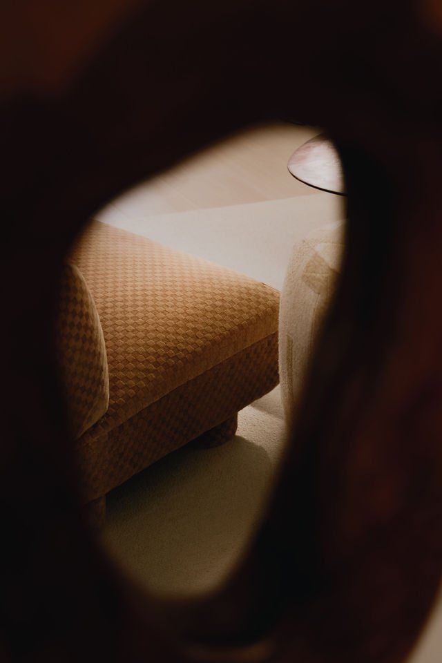 View through a small opening showing an armchair with a checkered pattern and part of a side table with a lamp.