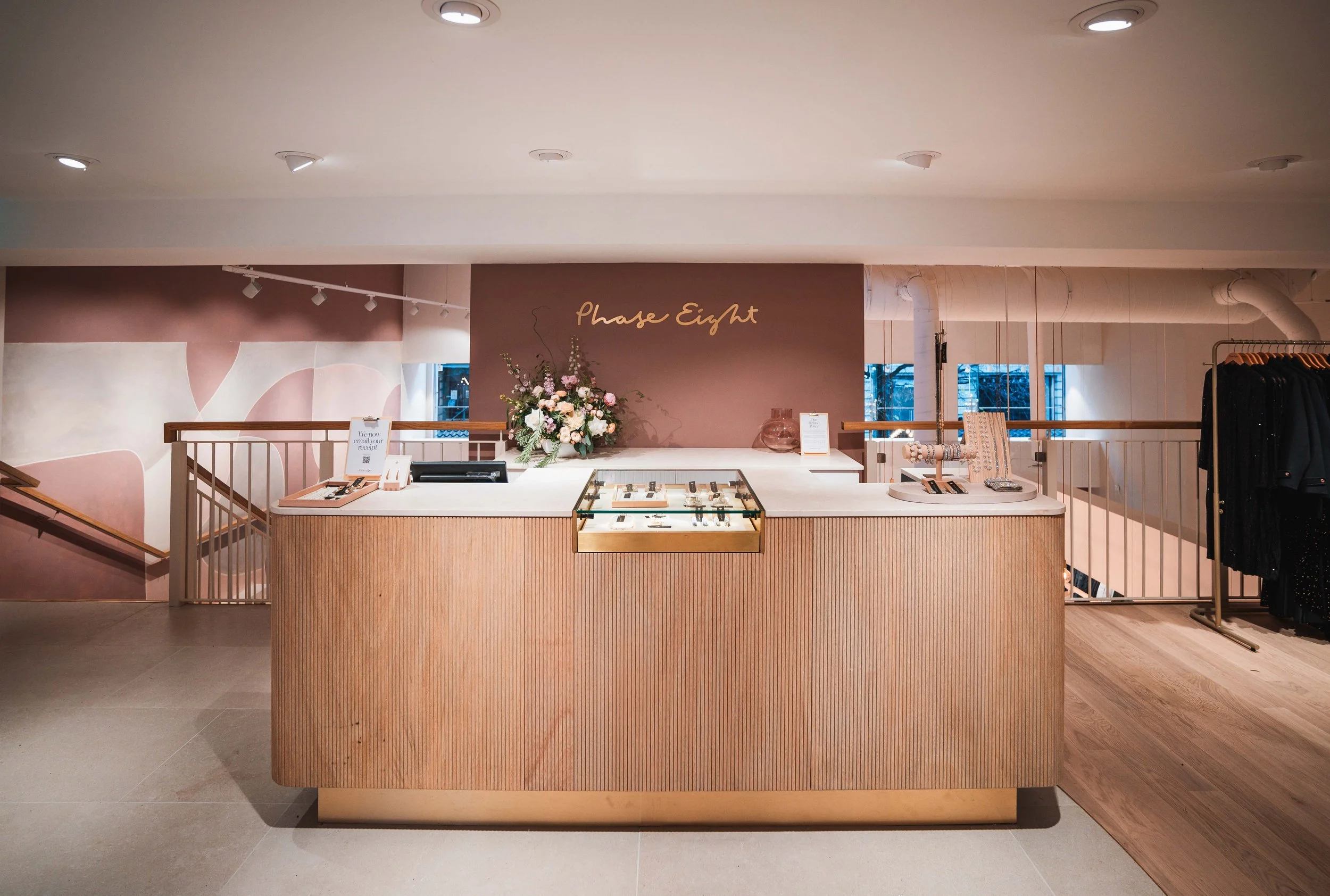 Jewelry display counter with flowers and jewelry inside a boutique with a sign that says 'Phase Eight' behind it.