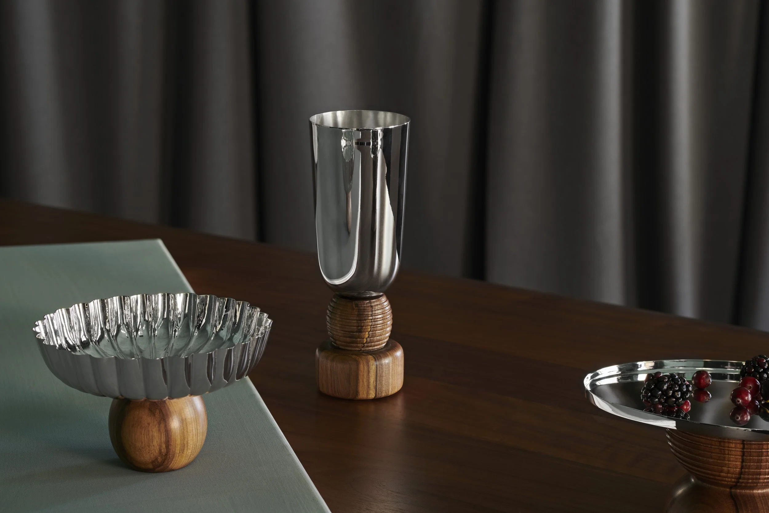 Decorative metal and wooden tableware on a dark wood table, with a dark curtain in the background