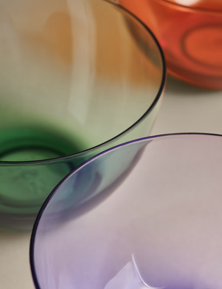 Close-up of three colorful, semi-transparent glass bowls in green, purple, and orange.