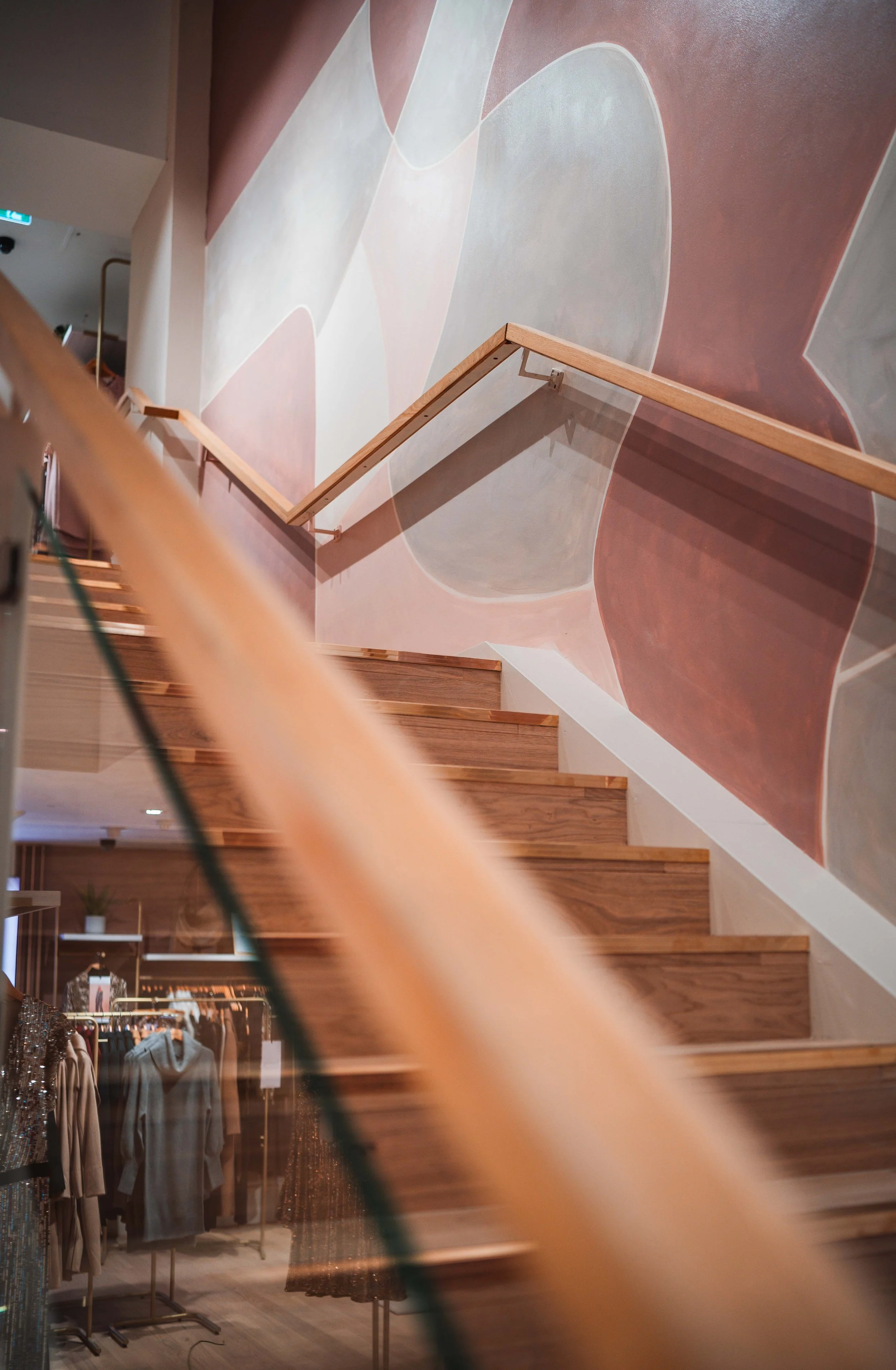 Wooden staircase inside a building with an abstract pink, gray, and white mural on the wall.