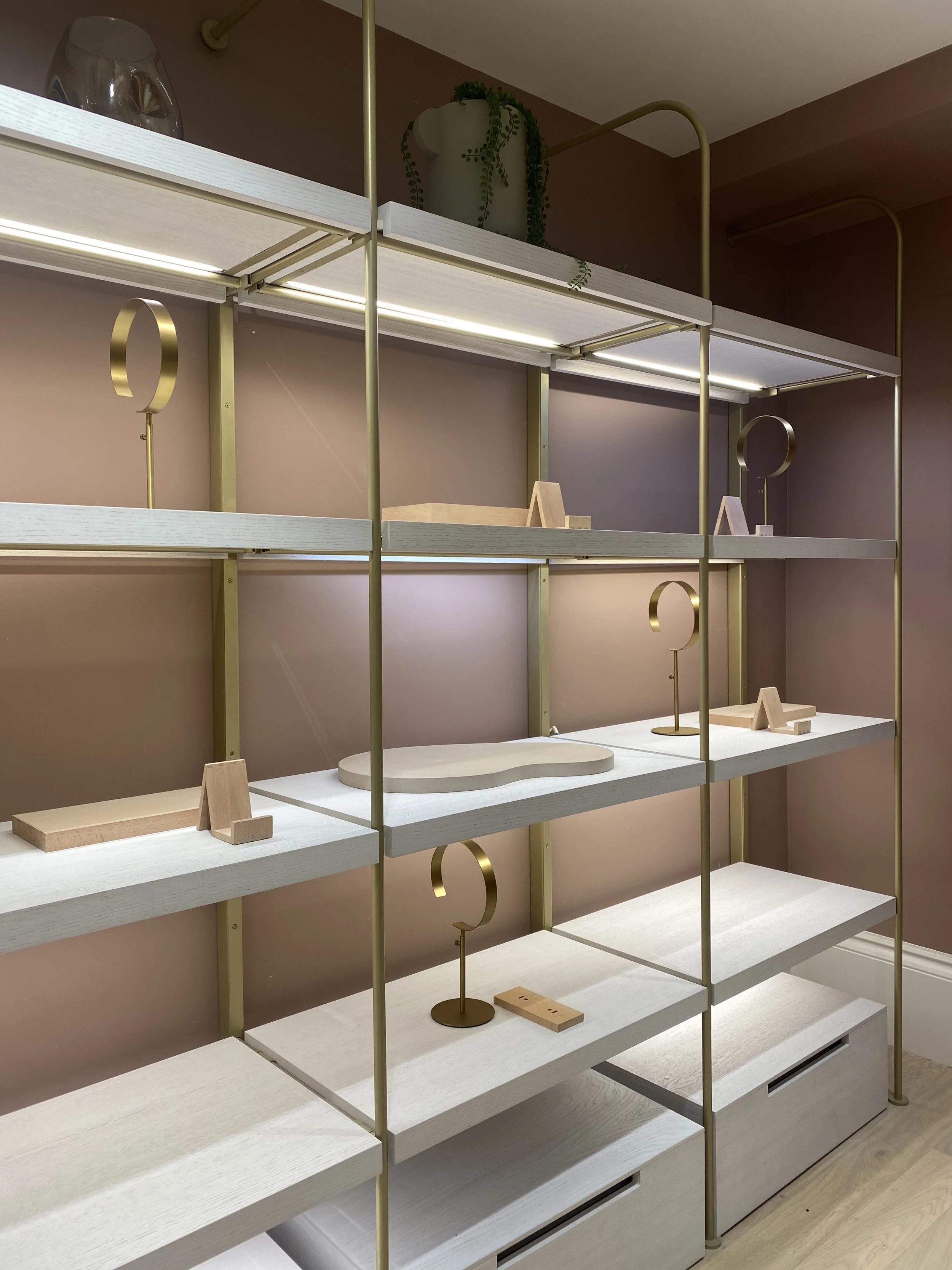 Empty white shelves with wooden decorative items and gold stand lamps against a pink wall.