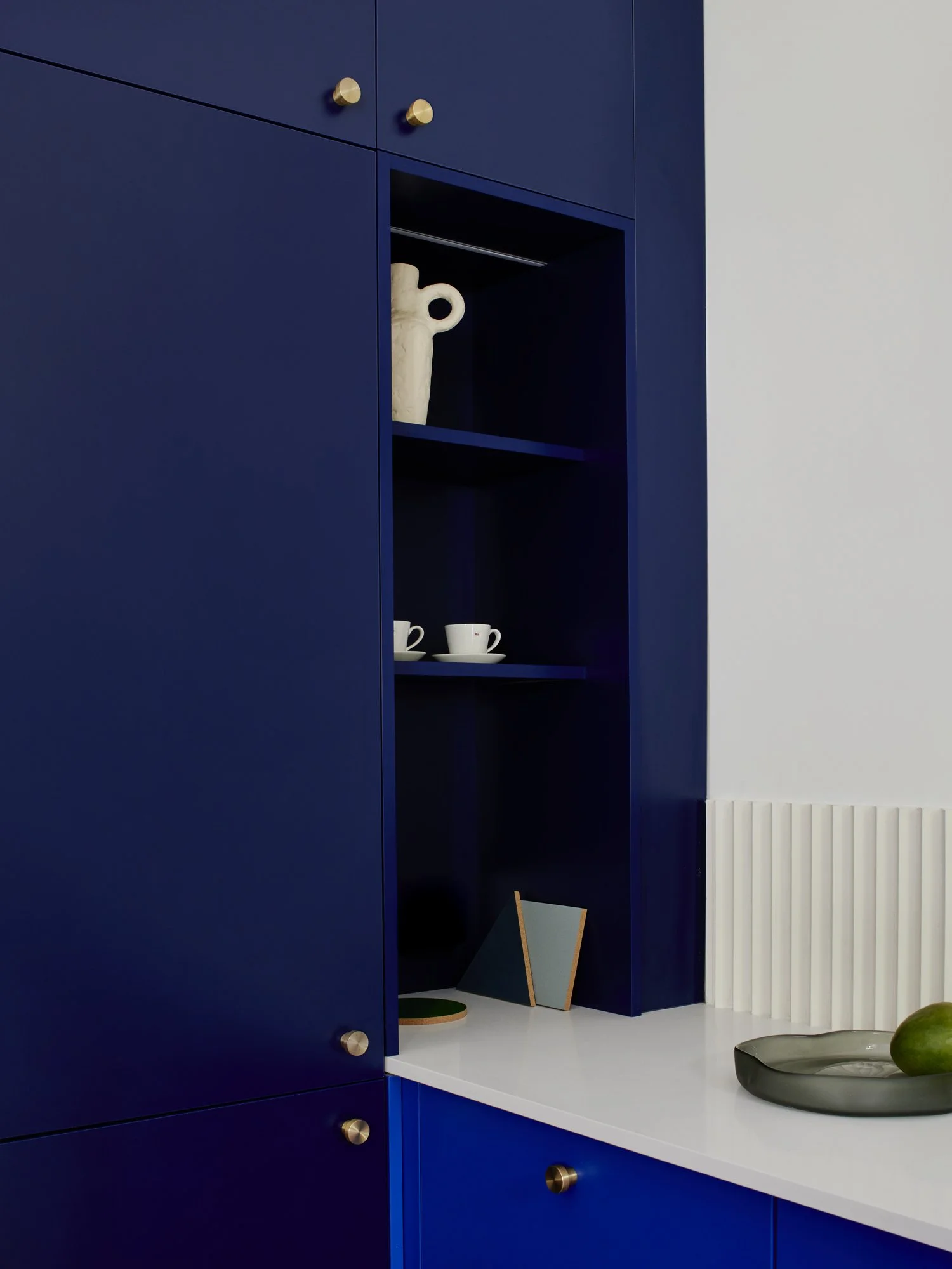 Close-up of a blue kitchen cabinet with gold knobs, displaying decorative items and dishes on the white countertop and interior shelves.