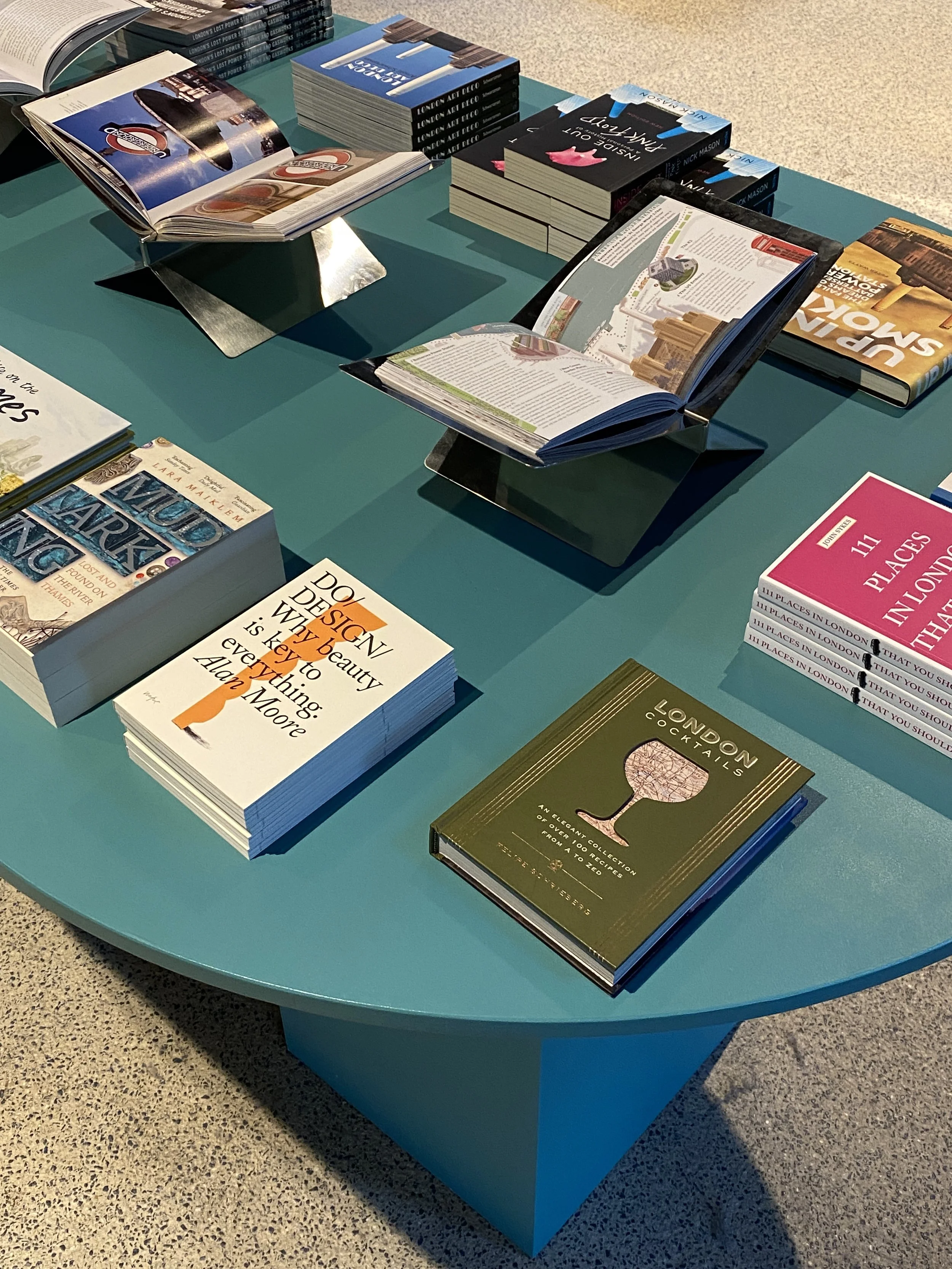 A display table with various hardcover and paperback books arranged on stands and laying flat, including travel guides, design, and city-themed books.