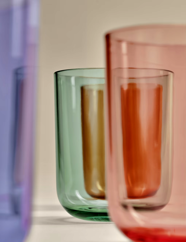 Colorful glass tumblers in purple, blue, green, yellow, orange, and pink, arranged in a row with focus on the middle glasses.
