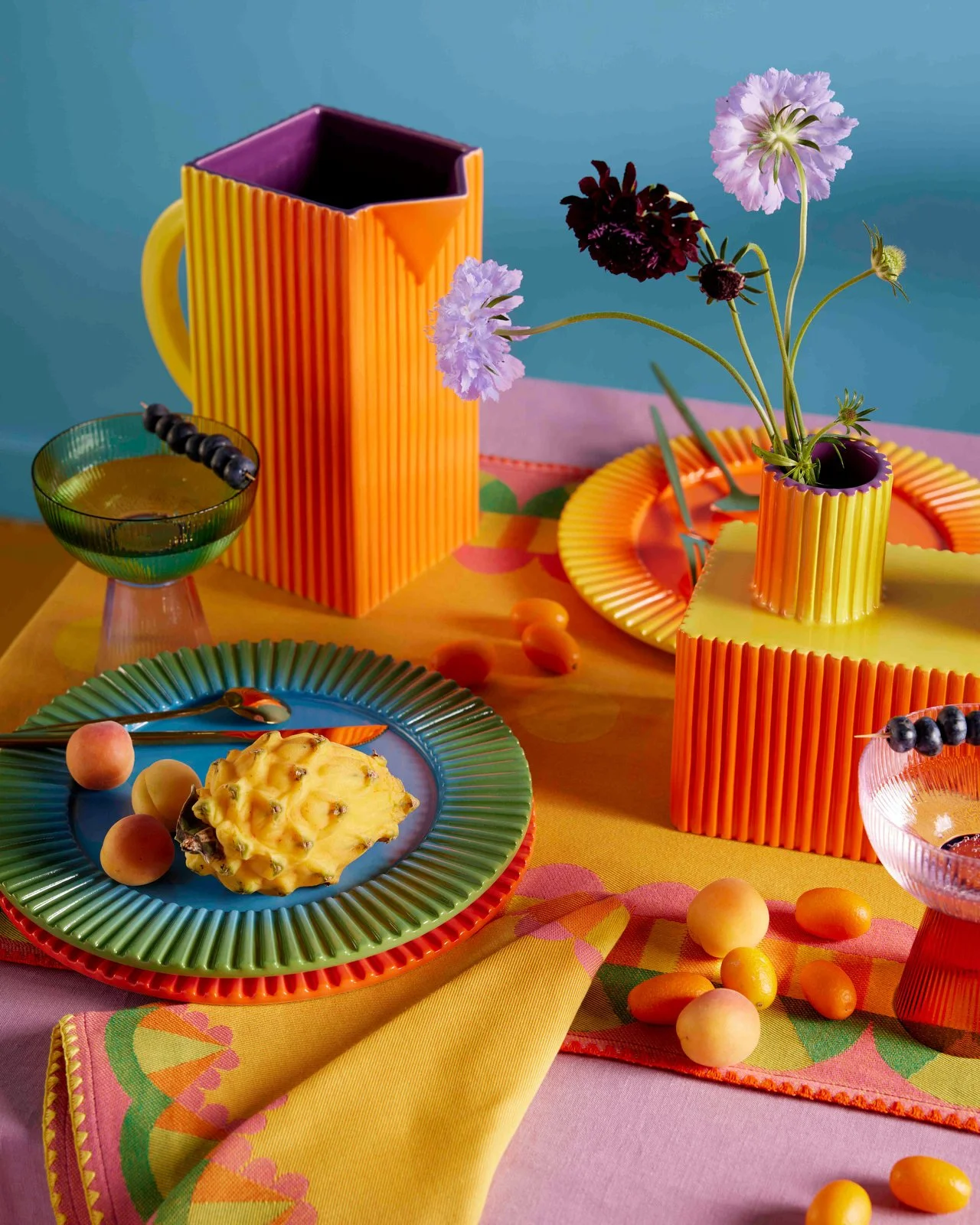 Colorful table setting with vibrant dishes, a pineapple, and flowers in a modern, bright style.